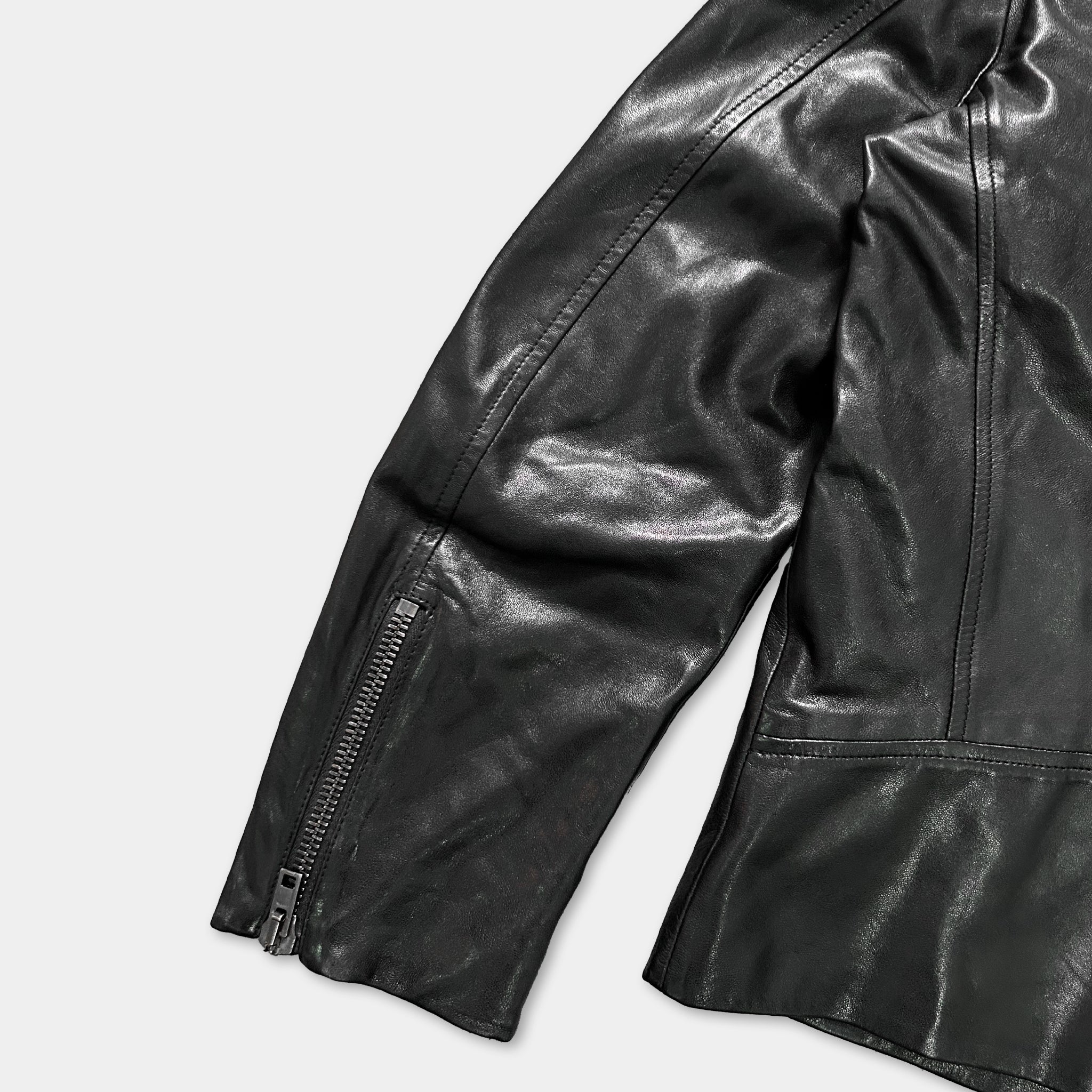 A close-up view of a black leather jacket, focusing on the zipper and the fabric.