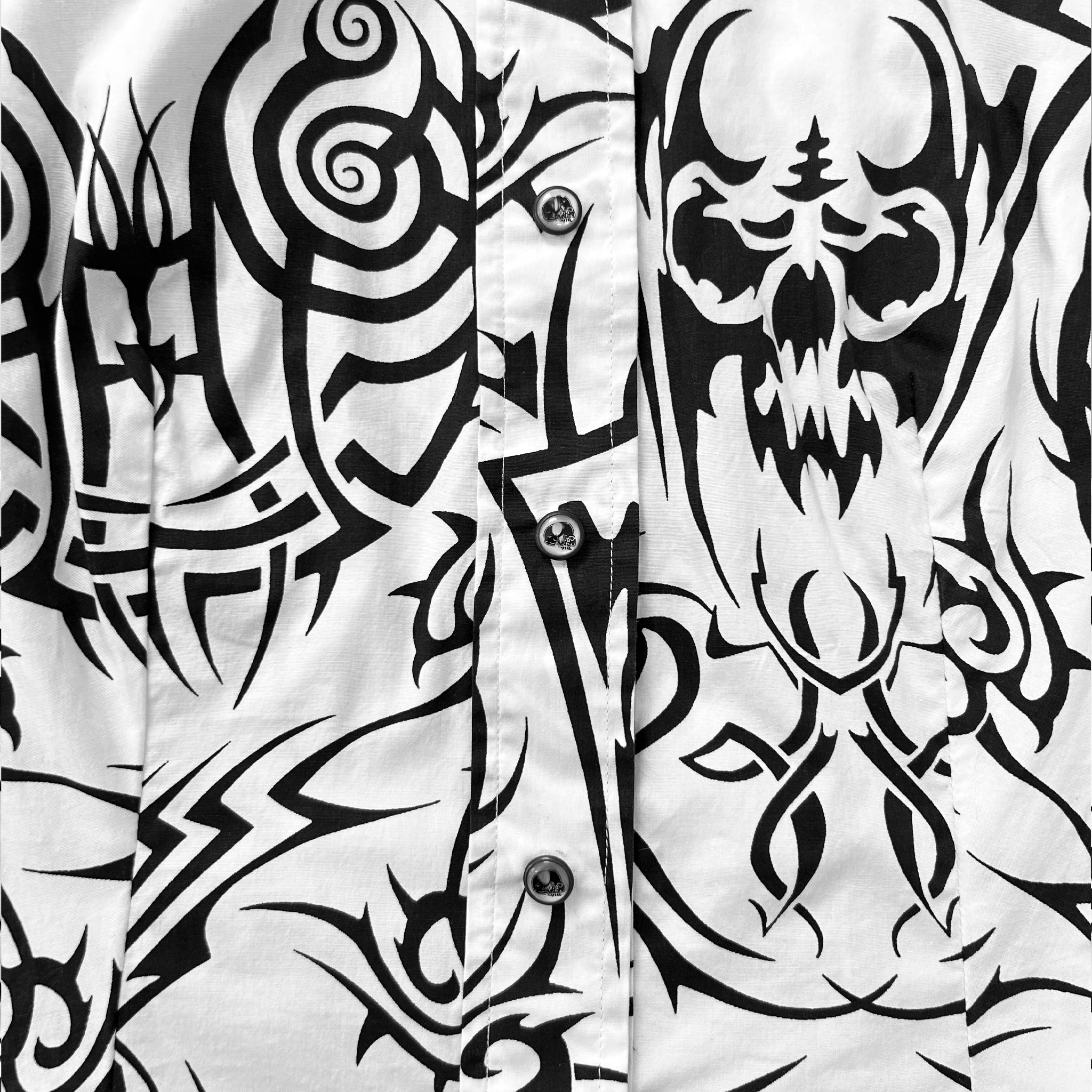a close-up view of a shirt with a black and white tattoo design. The design includes a skull and various other abstract patterns.