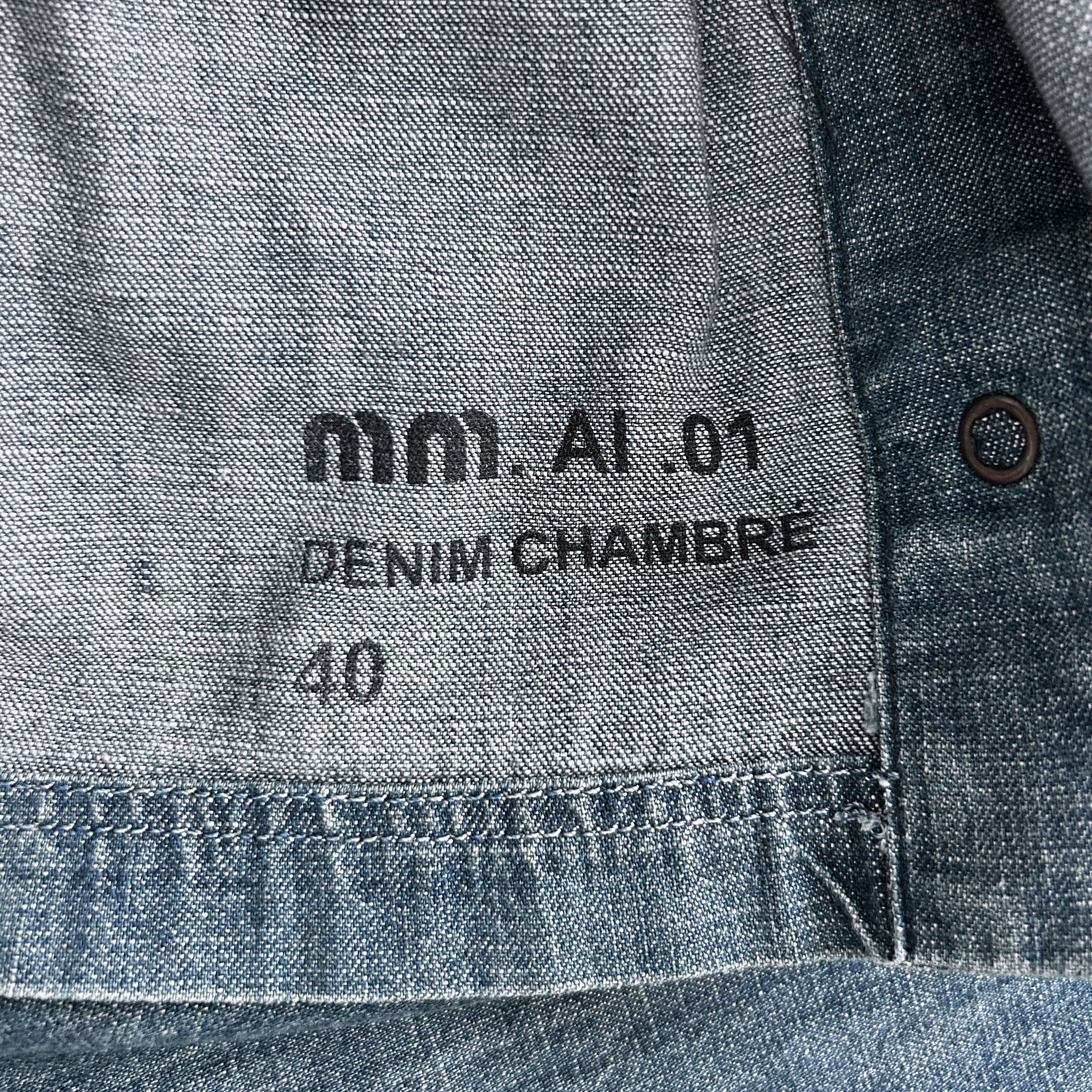 a close-up view of a denim fabric, possibly a pair of jeans, with text printed on it. The text appears to be in French and reads "mm. A1.01 Denim Chambre 40".