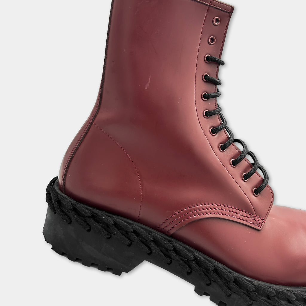 A close-up view of a red leather boot with black laces and a black rubber sole.