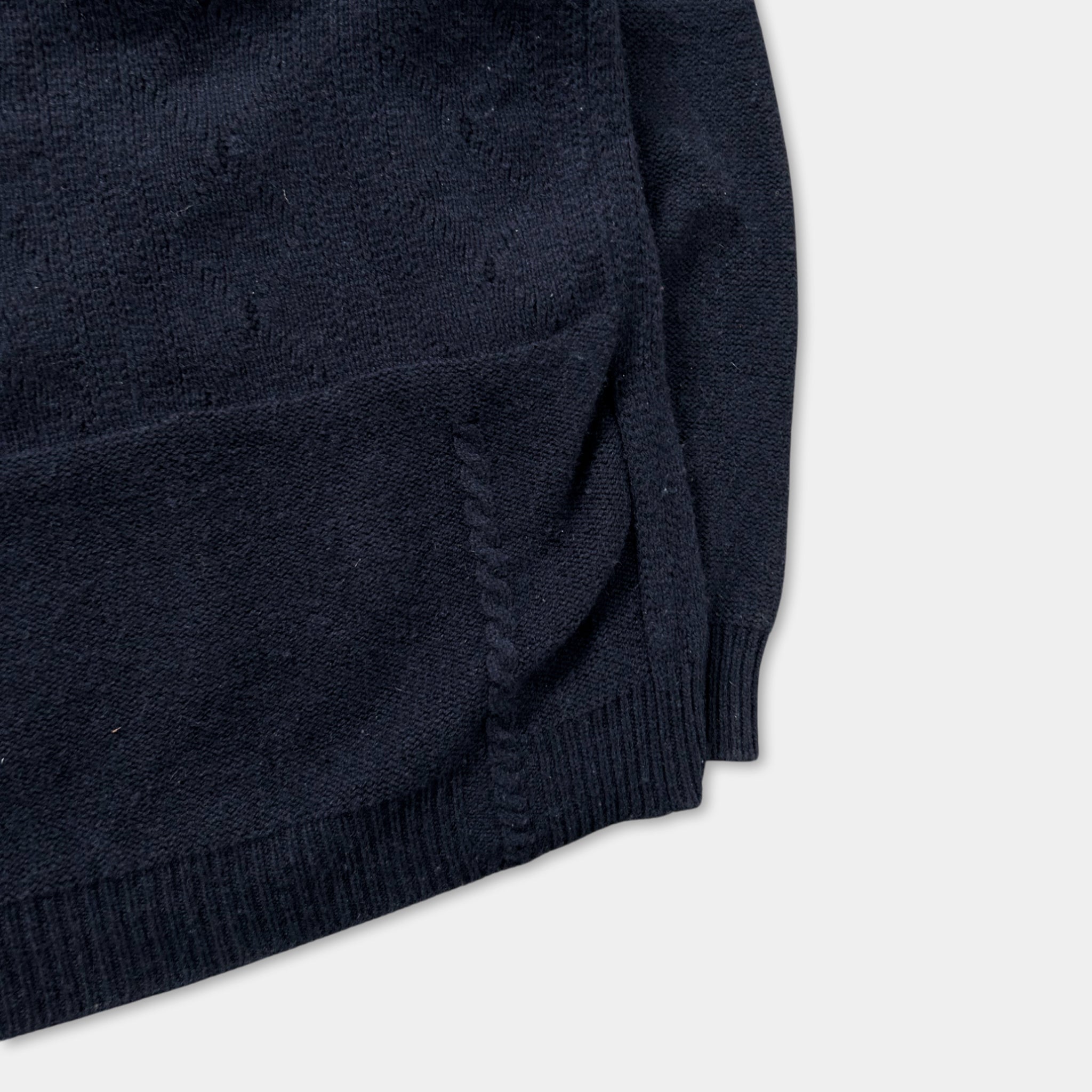 A close-up view of a navy blue knitted sweater with visible stitching and a small pocket on the front.