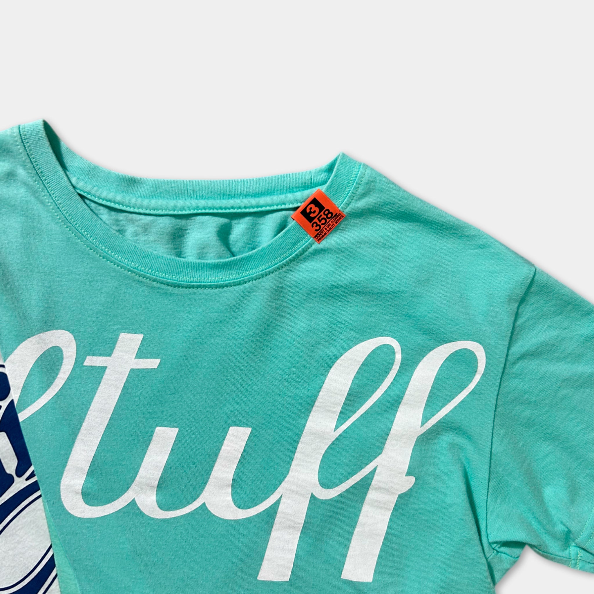 A turquoise t-shirt with the word "stuff" printed in white letters.