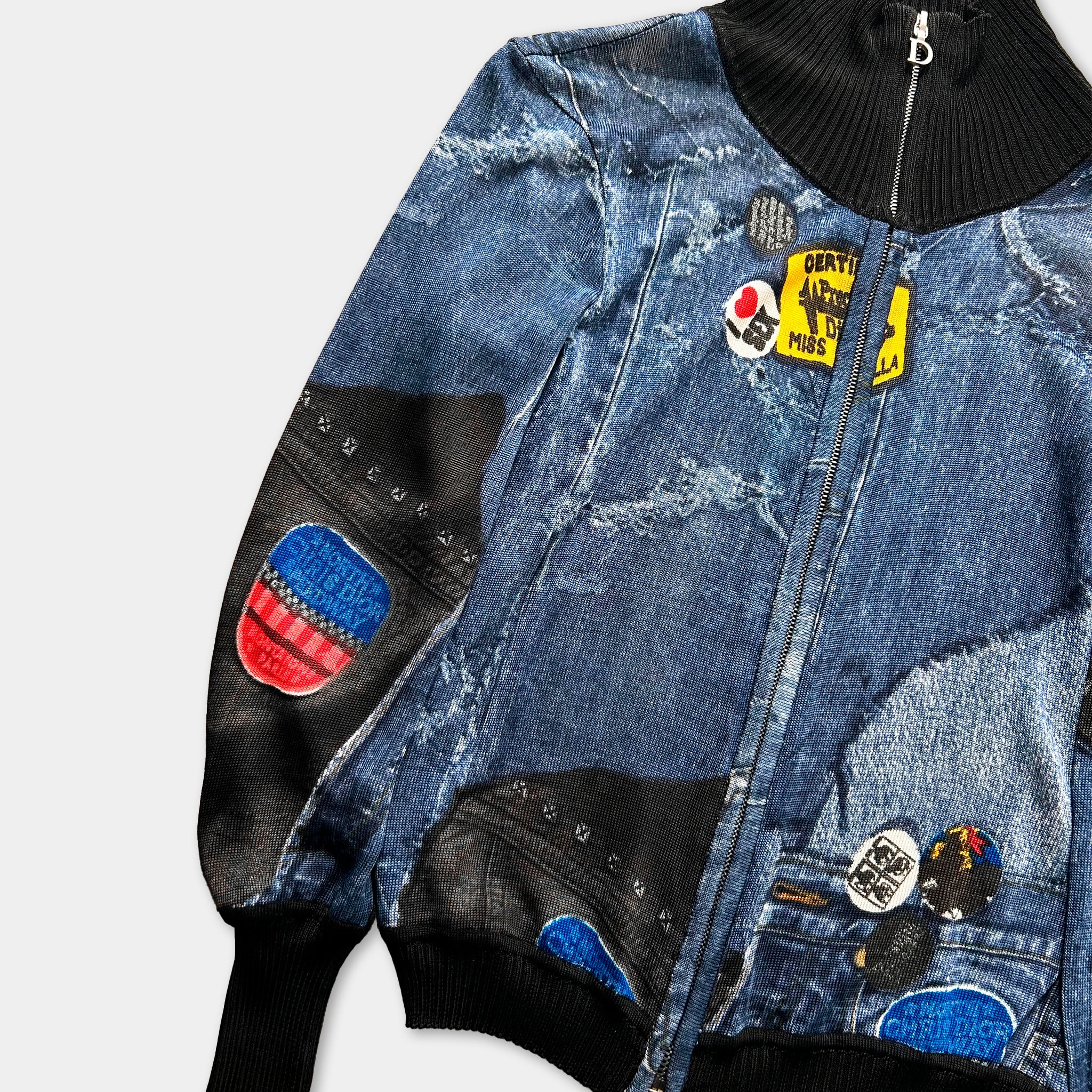 A close-up view of a denim jacket with various patches and designs, including a zipper and a collar.