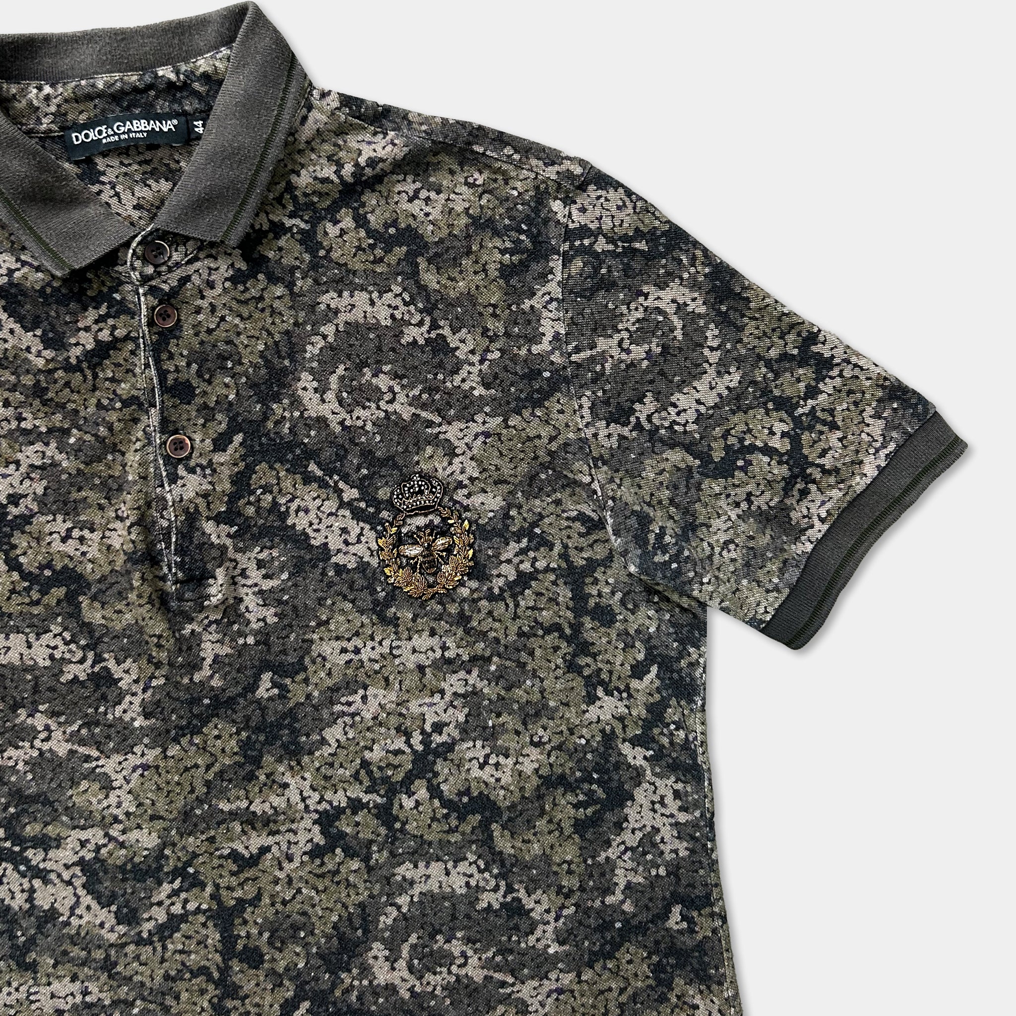 A camouflage-patterned polo shirt with a gold emblem on the left side.