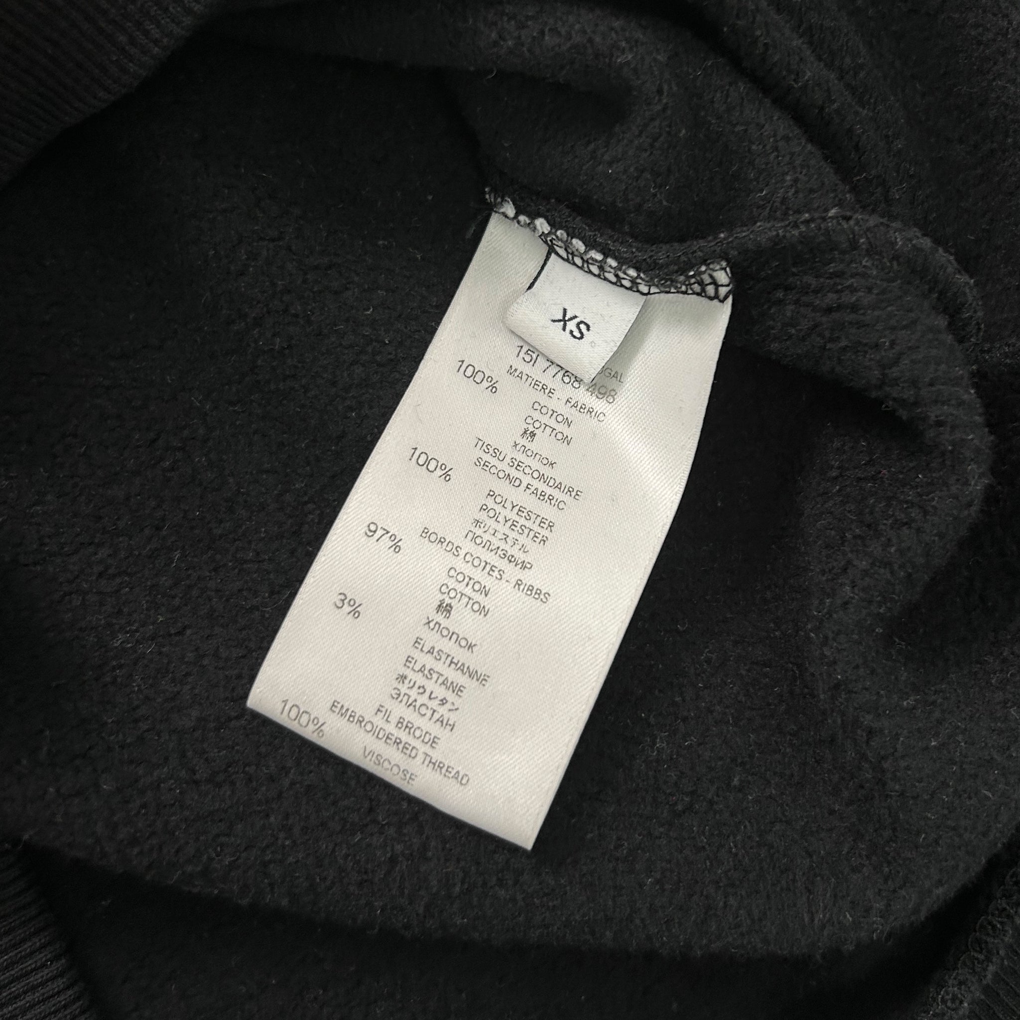 a close-up view of a black fabric, possibly a sweater or garment, with a white label attached to it. The label contains text and numbers, likely providing information about the fabric, such as the material, weight, and other specifications.