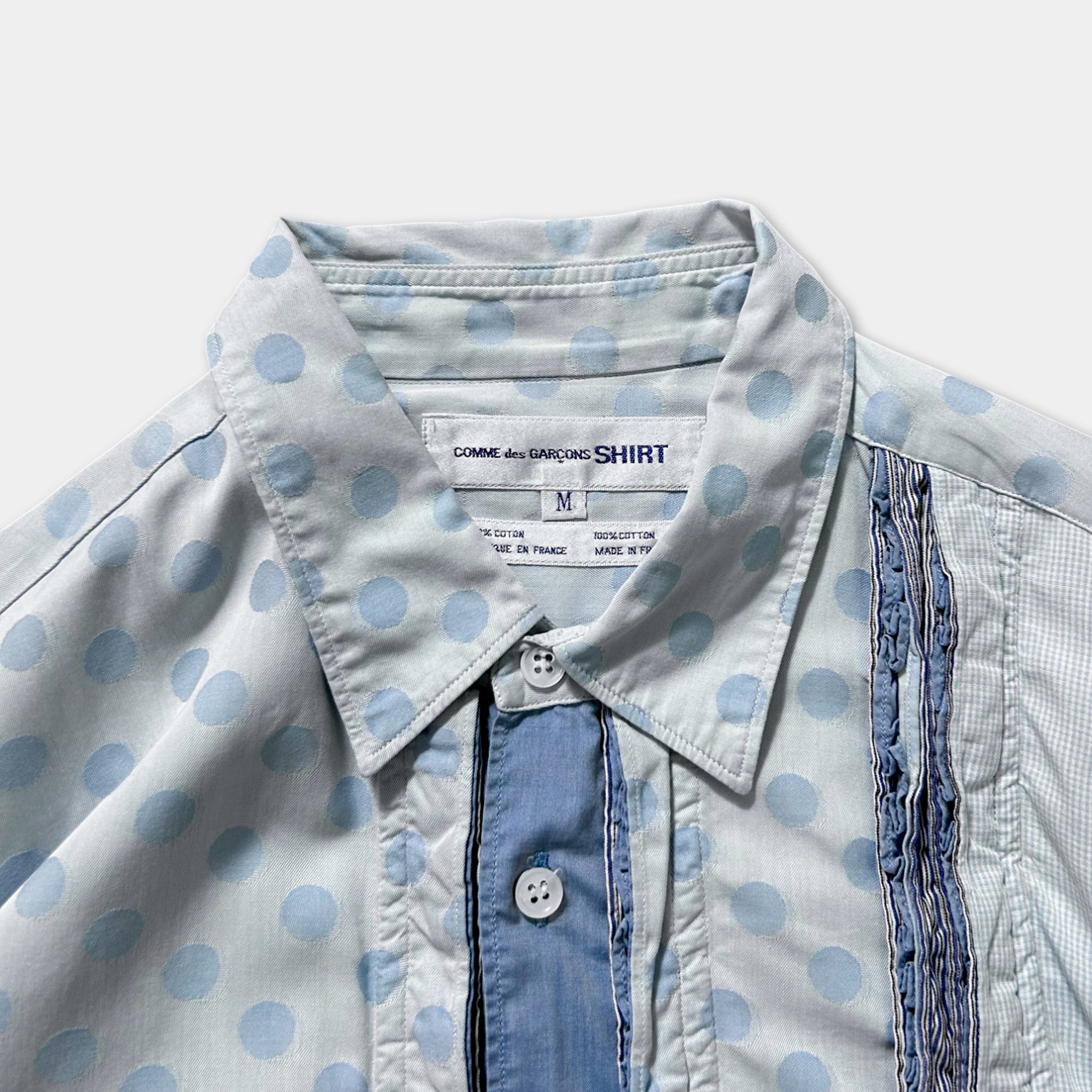 a close-up view of a white polka dot shirt with a blue collar and buttons.