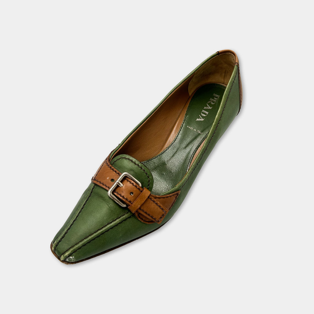 A green leather shoe with a brown leather strap and buckle detail.