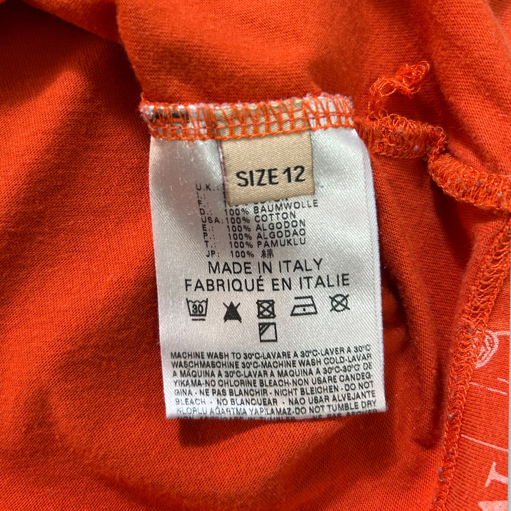 a close-up view of a red fabric, possibly a t-shirt or garment, with a label attached to it. The label provides information about the size, material, and care instructions for the fabric.