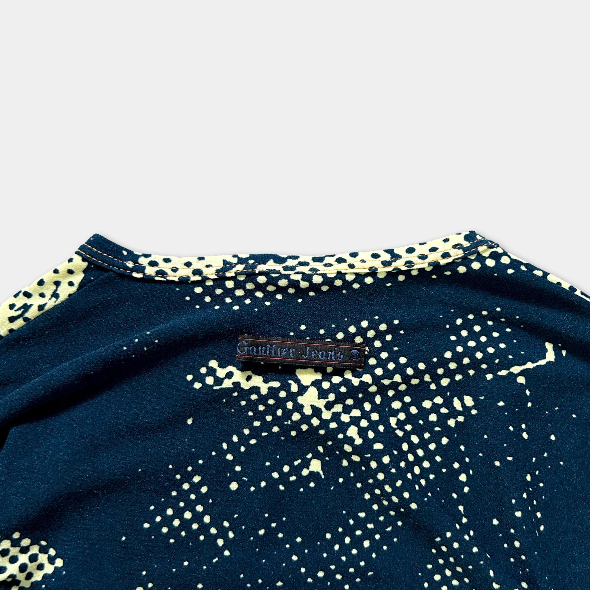 a close-up view of a dark blue shirt with a yellow polka dot pattern. There is a small black label on the shirt with text that reads "Gauffin Jeans".