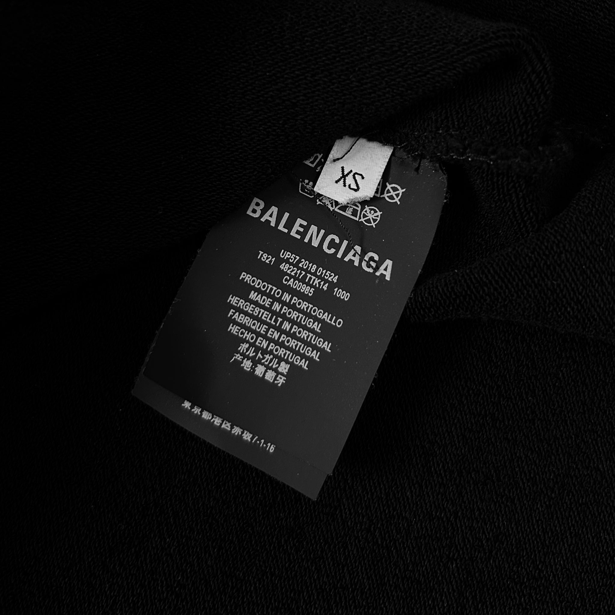A black label with white text on a black background, attached to a black fabric.