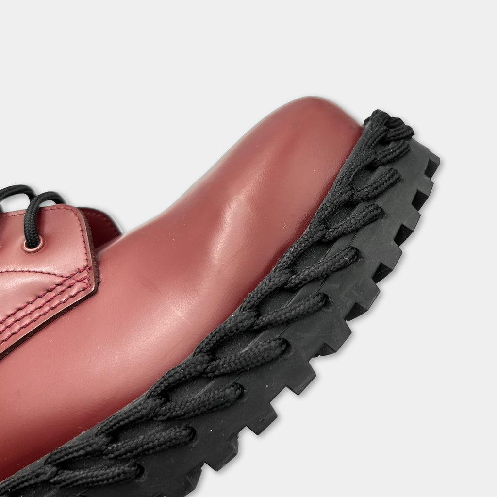 A close-up view of a red leather shoe with a black rubber sole, showcasing the shoe's design and texture.