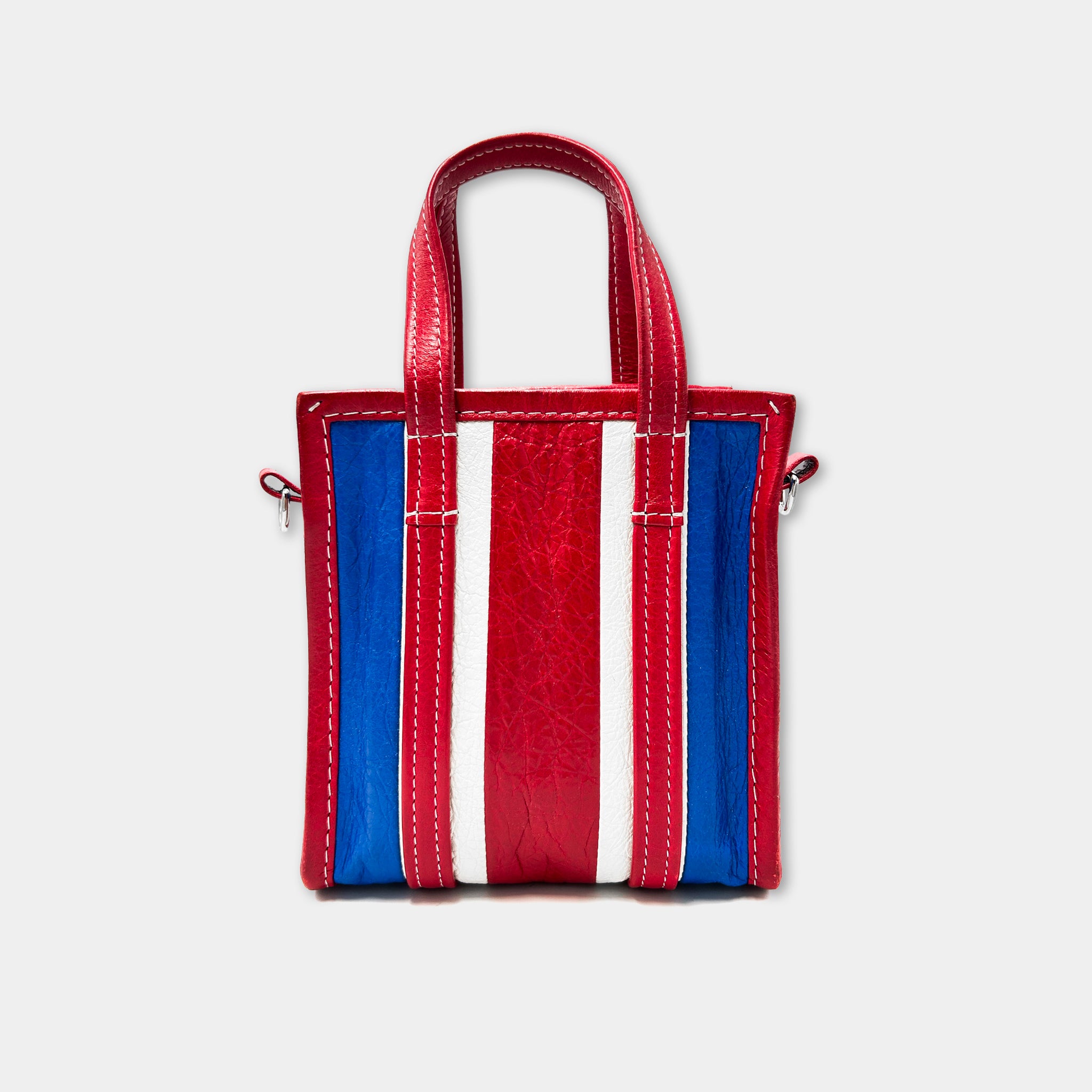 A red, blue, and white striped handbag with a red handle and straps.
