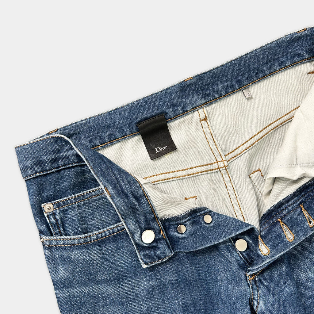 A pair of blue jeans with a Dior brand tag visible inside the pocket.
