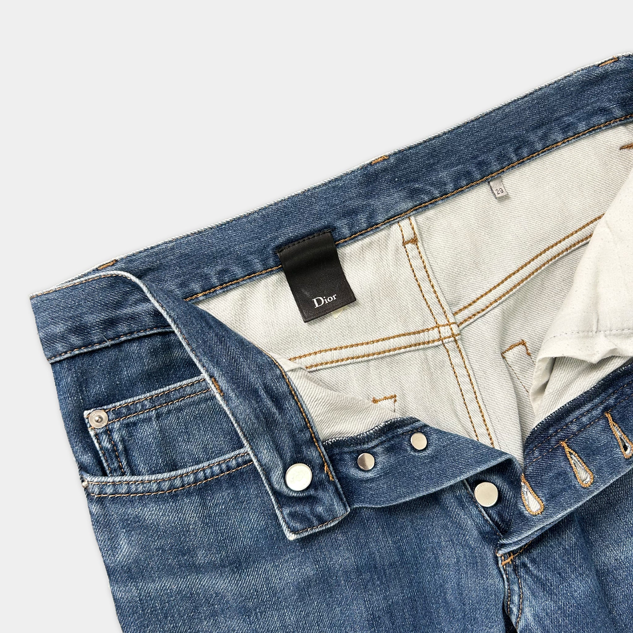 A pair of blue jeans with a Dior brand tag visible inside the pocket.