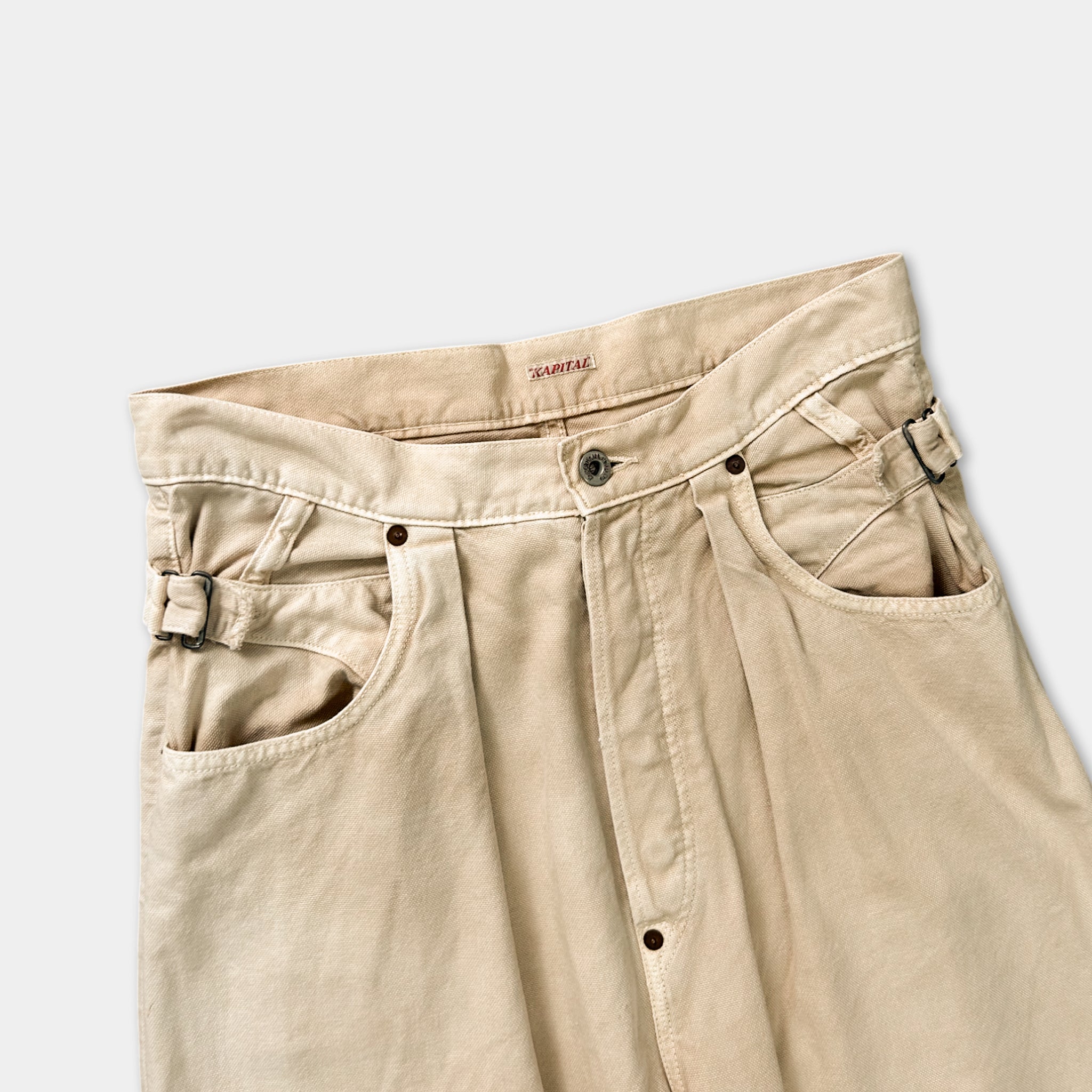A pair of khaki-colored jeans with a button waistband and a small zipper pocket on the front.