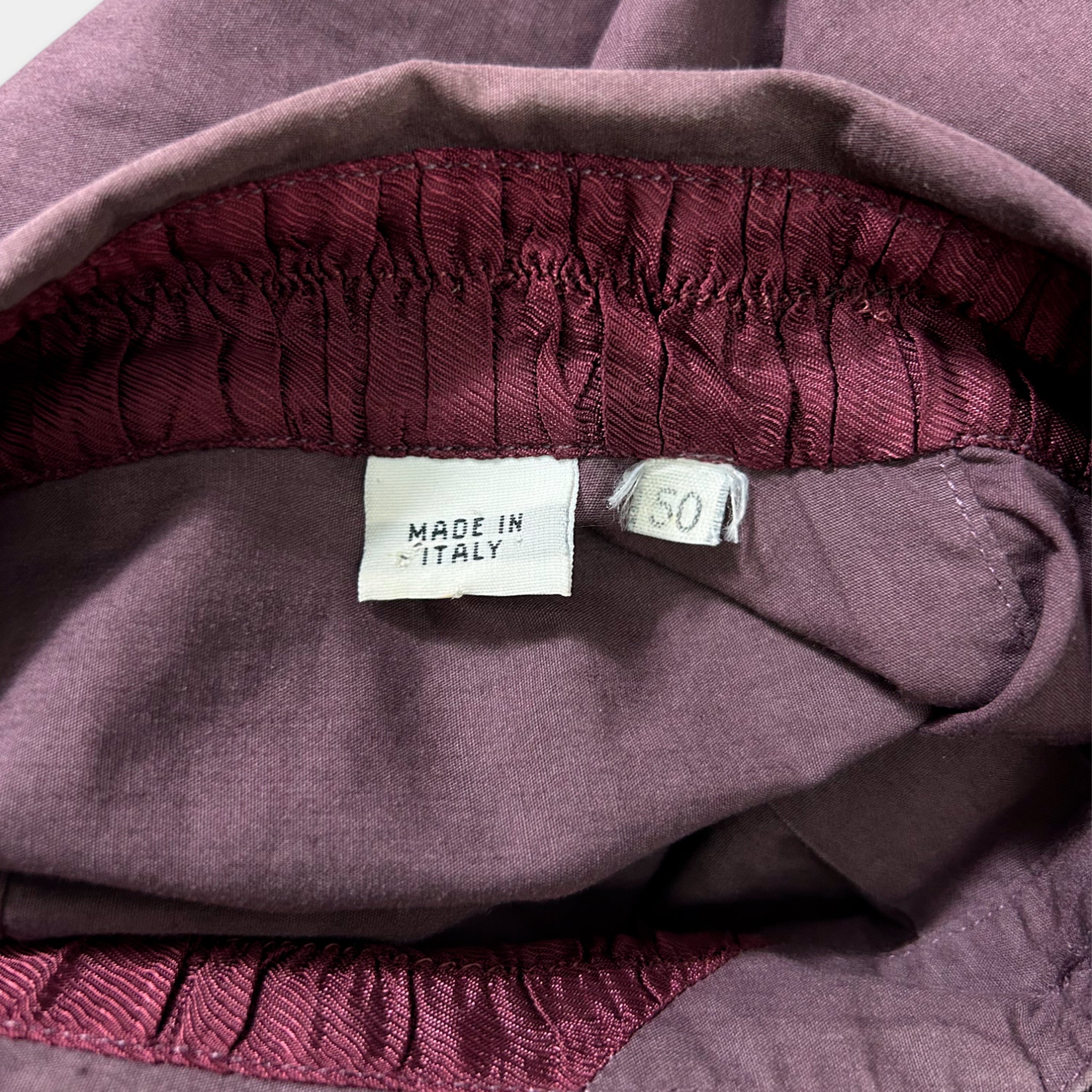 a close-up view of a purple fabric, possibly a garment or textile, with a label indicating that it is made in Italy.