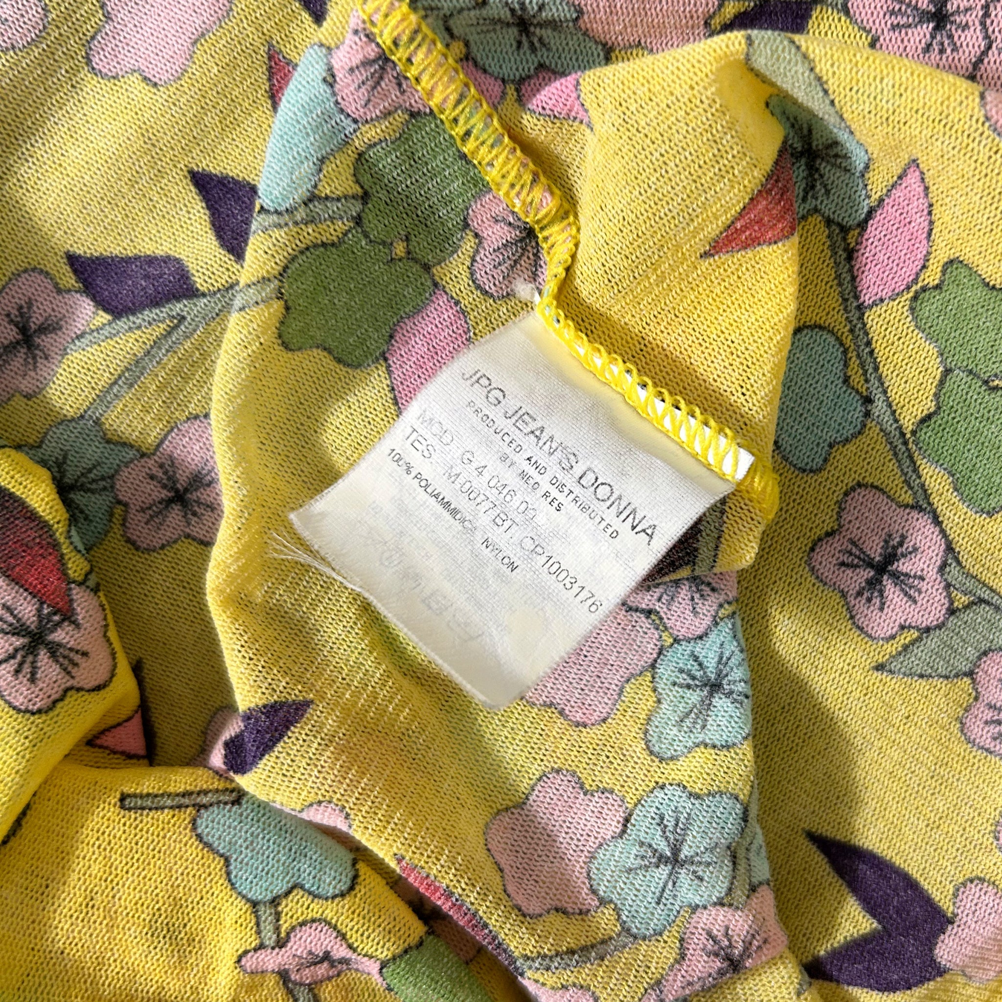 a close-up view of a yellow fabric with a floral pattern, featuring a white label with text on it.