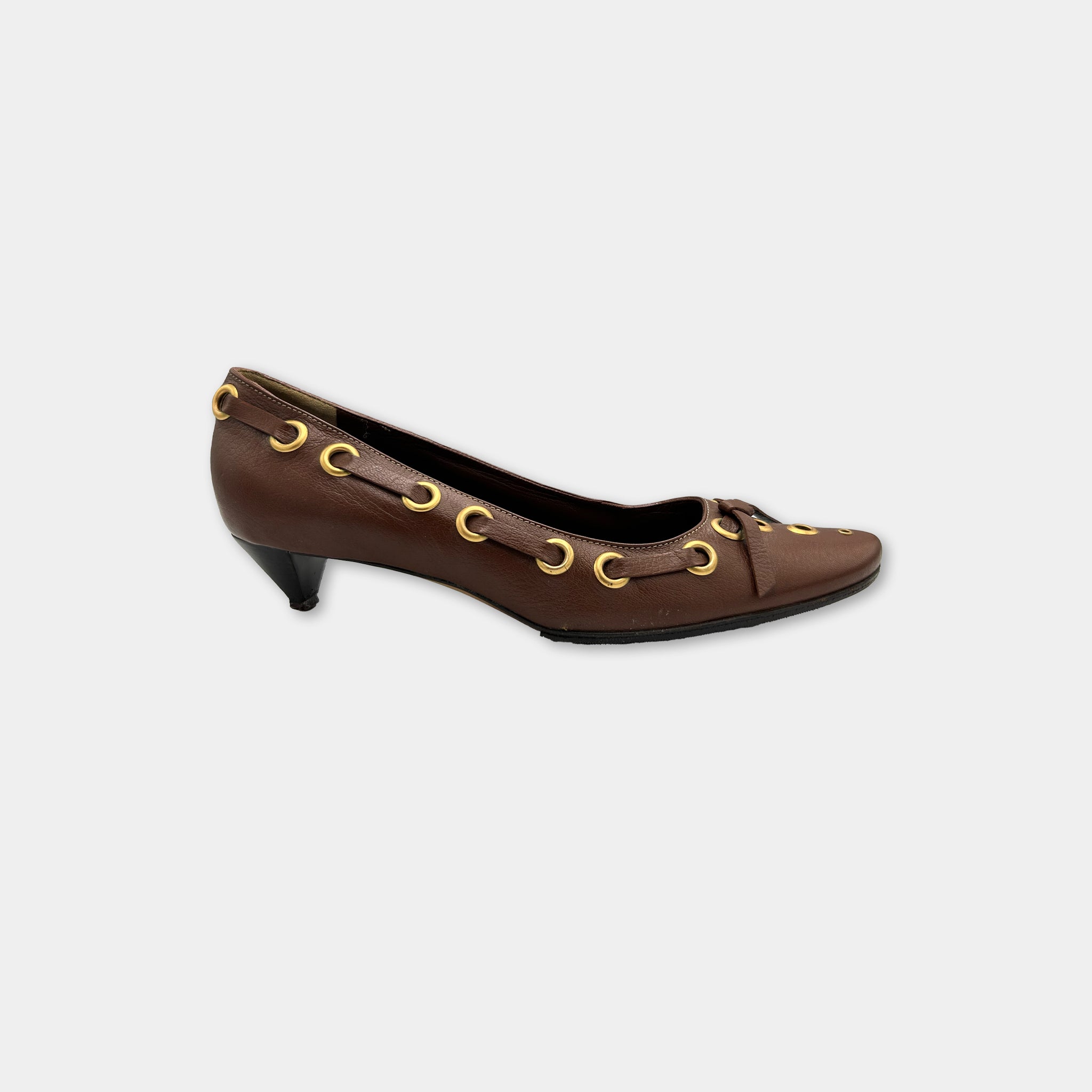A brown leather high-heeled shoe with gold-colored metal studs on the toe and heel.