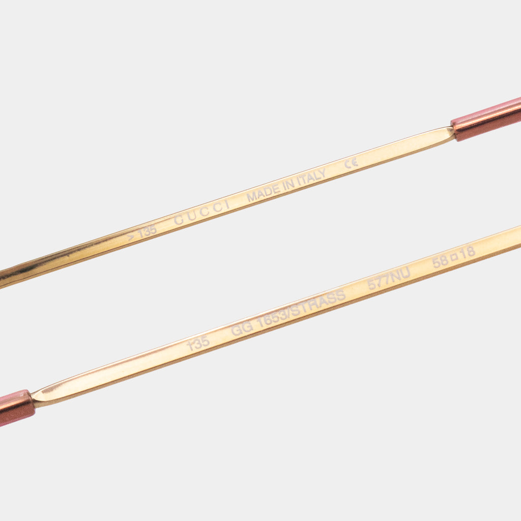 a pair of gold-colored sunglasses with a red frame. The text on the frame indicates that the sunglasses are made in Italy and are a Gucci product.