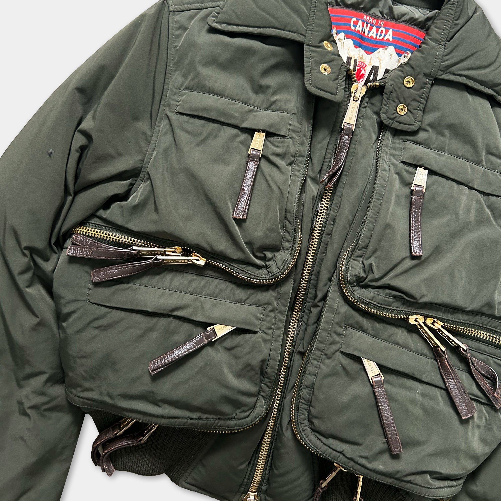 A dark green jacket with multiple zippers and pockets, featuring a red and blue label on the collar.