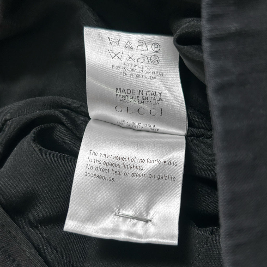 a close-up view of a Gucci clothing label, with a black fabric visible underneath. The label contains text and symbols indicating the brand and product information.
