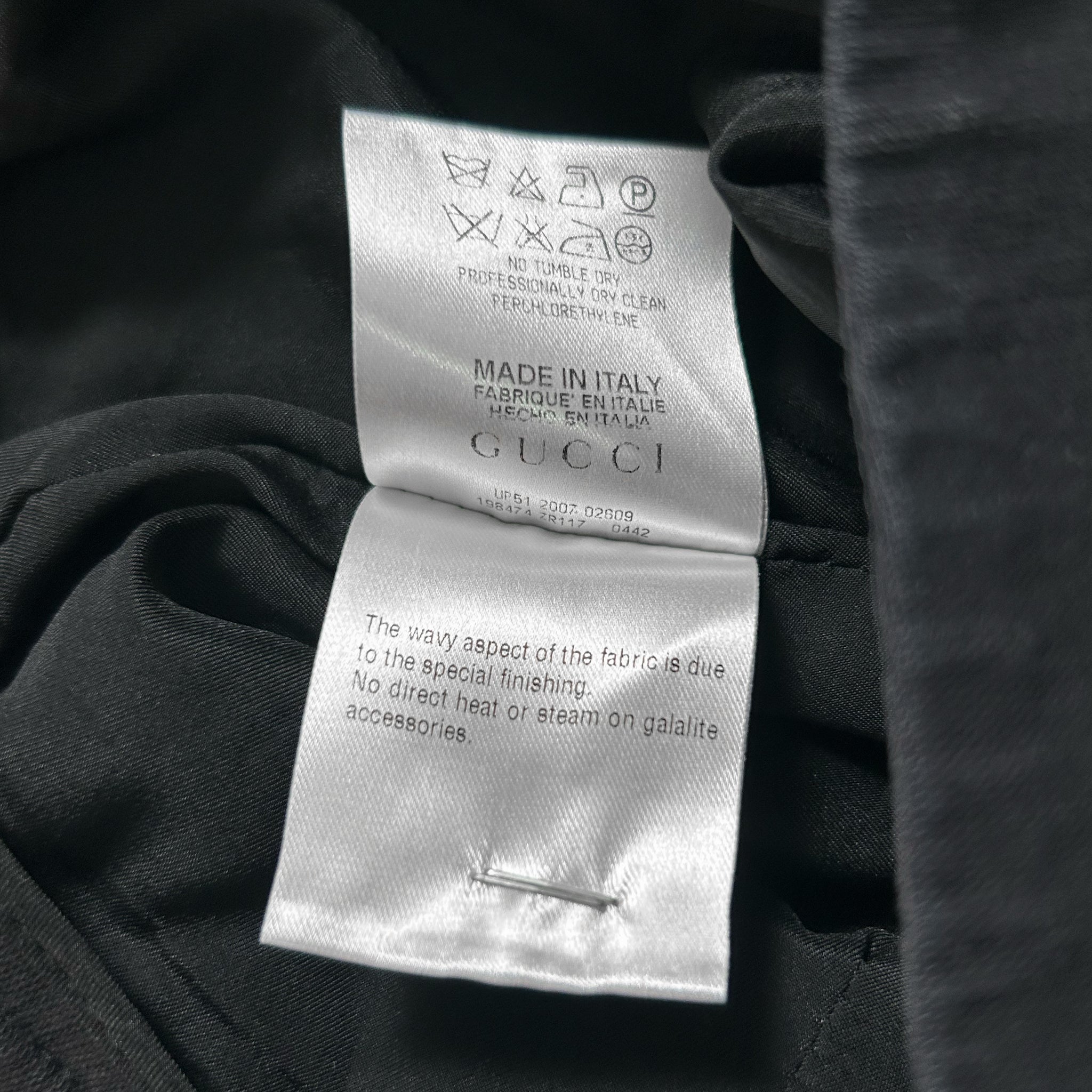 a close-up view of a Gucci clothing label, with a black fabric visible underneath. The label contains text and symbols indicating the brand and product information.