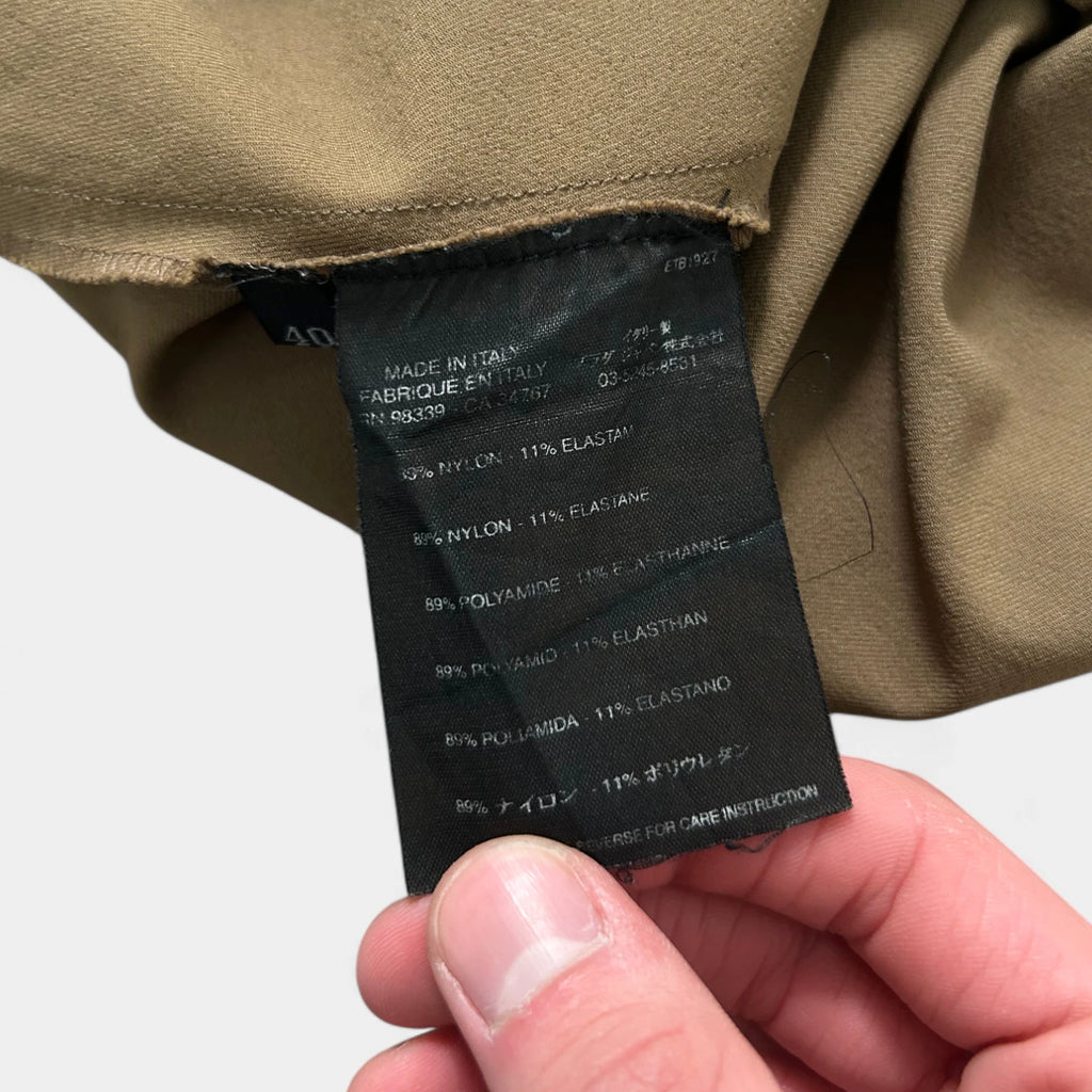 A person is holding a black label with text on it, which appears to be a garment label.
