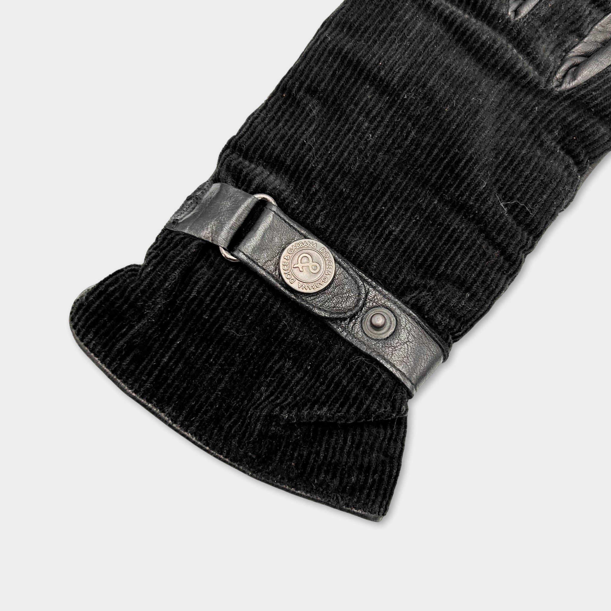 A close-up view of a black glove with a metal buckle and a black strap.
