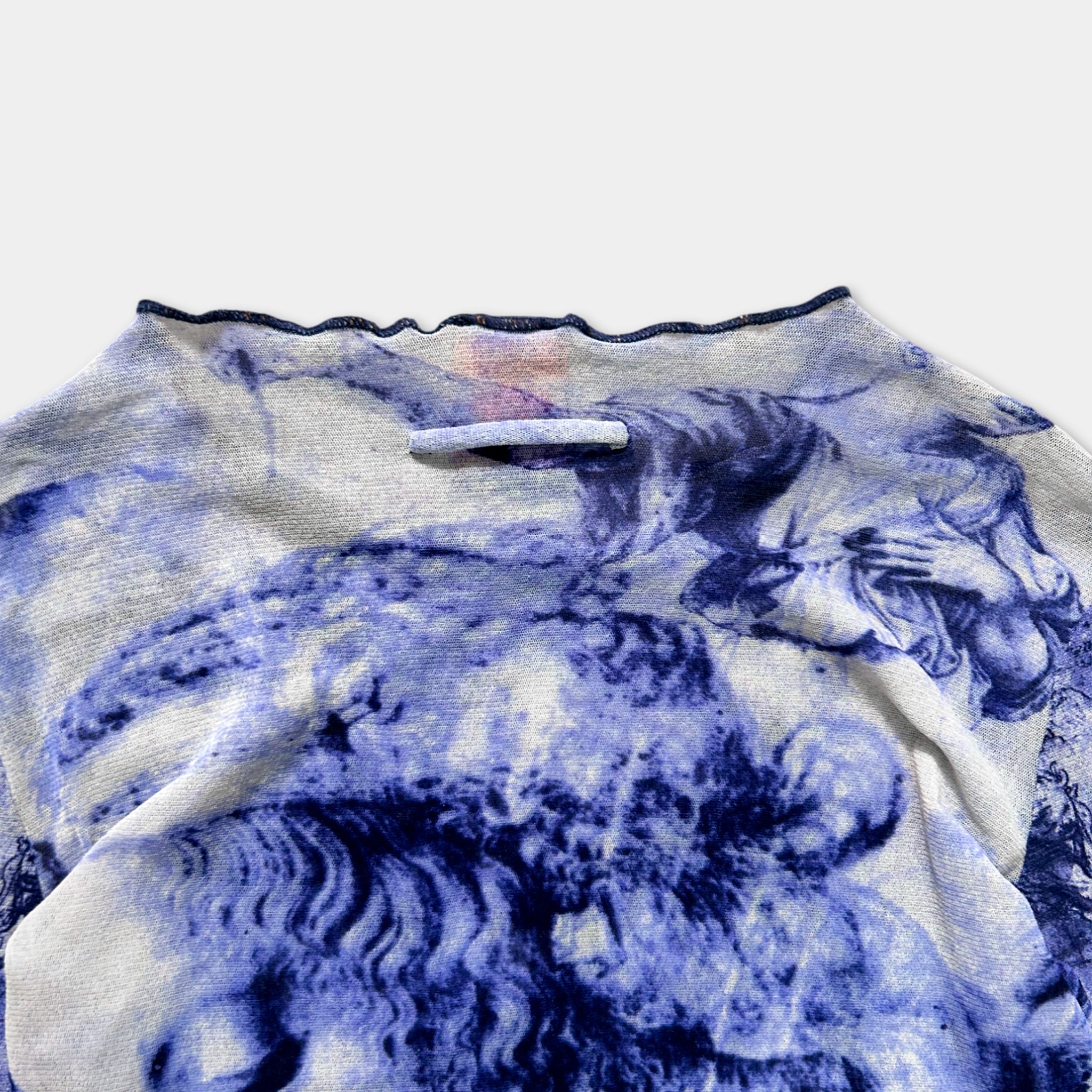a close-up view of a blue and white patterned fabric, possibly a sweater or a garment, with a small handle or zipper pull attached to the top.