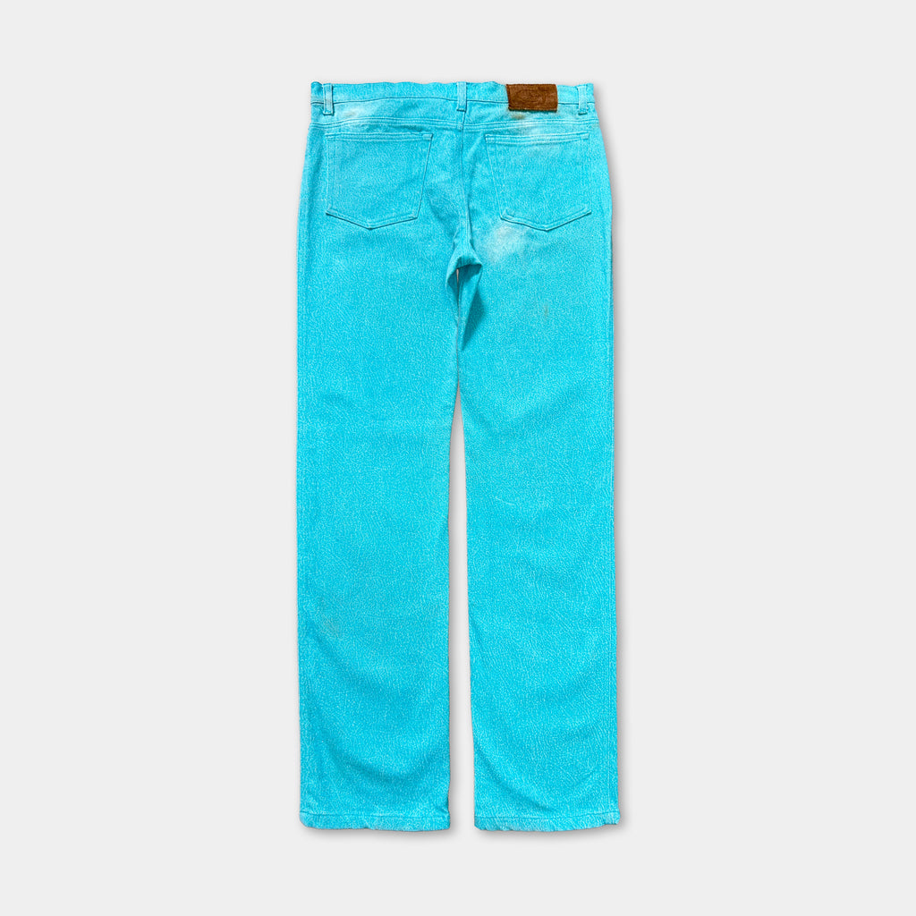 A pair of bright turquoise-colored jeans with a brown leather patch on the back pocket.