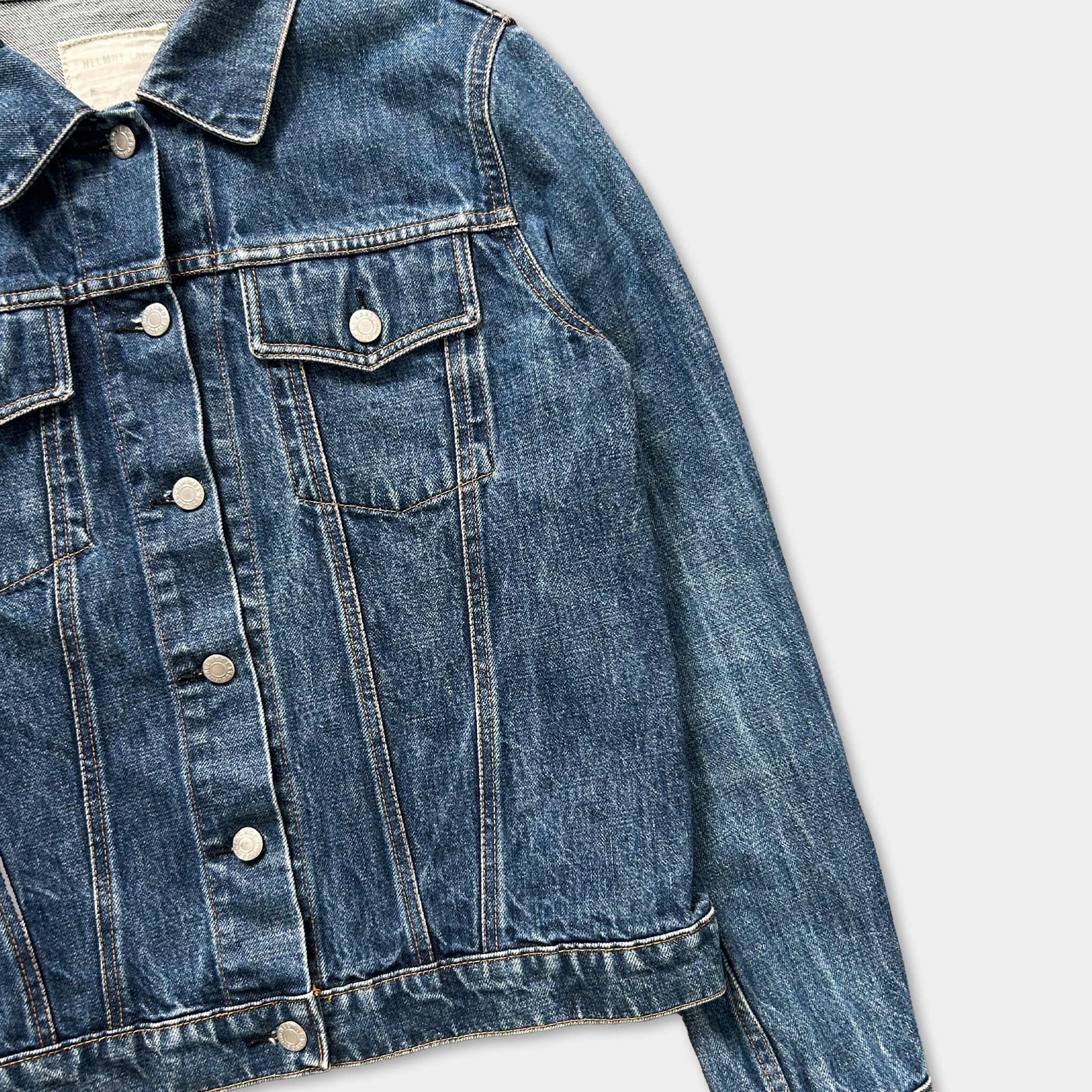 A close-up view of a blue denim jacket with a button-down front and two pockets.