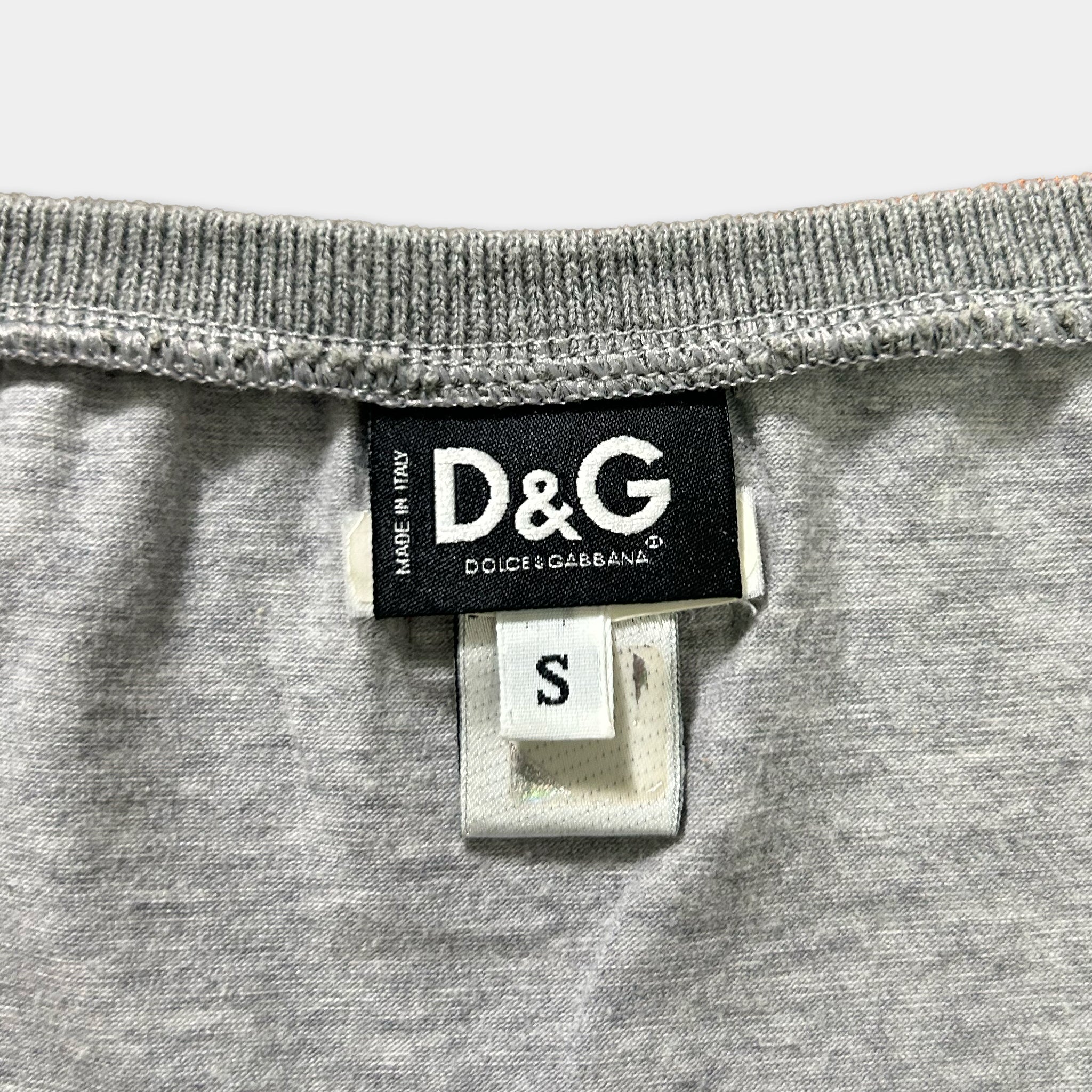 A close-up view of a grey fabric, likely a garment, with a label attached to it. The label displays the text "D&G" and "DC/G GABBANA".