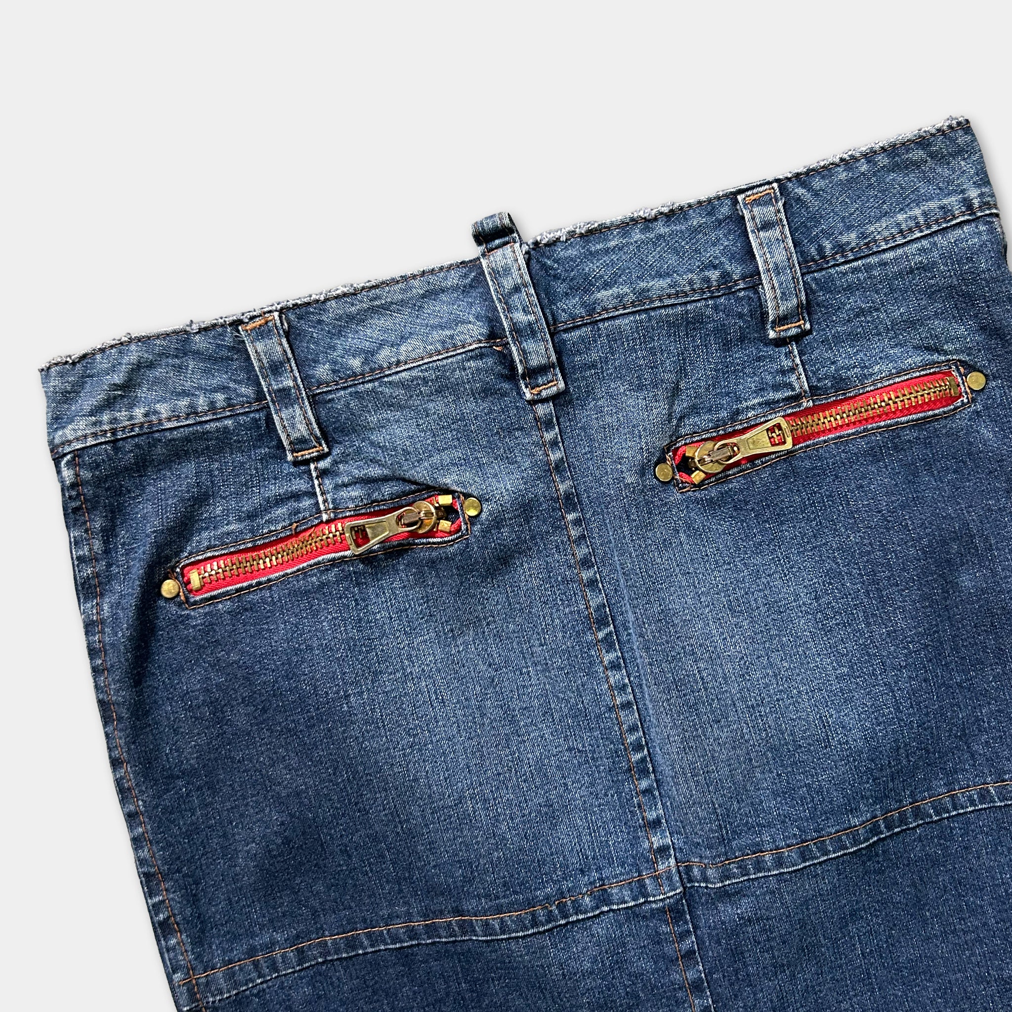 A pair of blue jeans with red zipper pulls and gold hardware.
