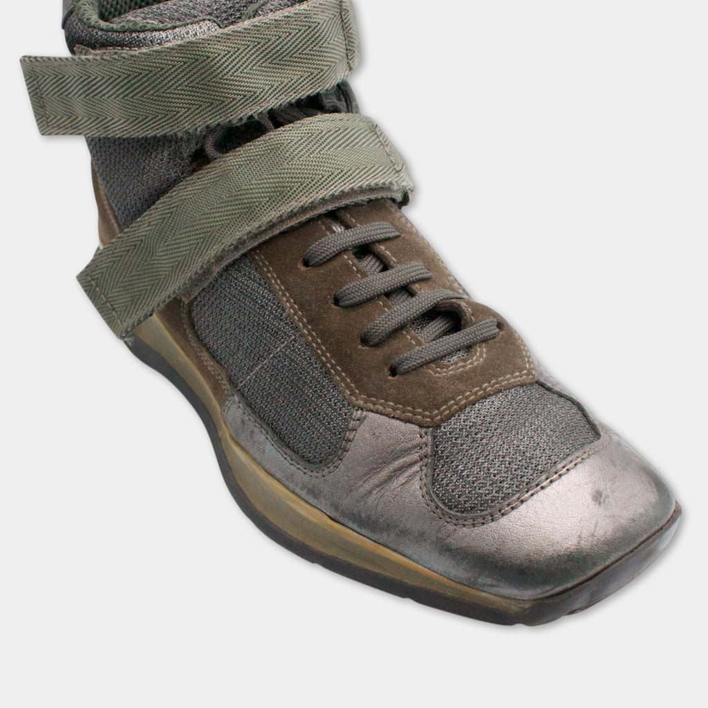 A close-up view of a brown and gray athletic shoe with a green strap and laces.
