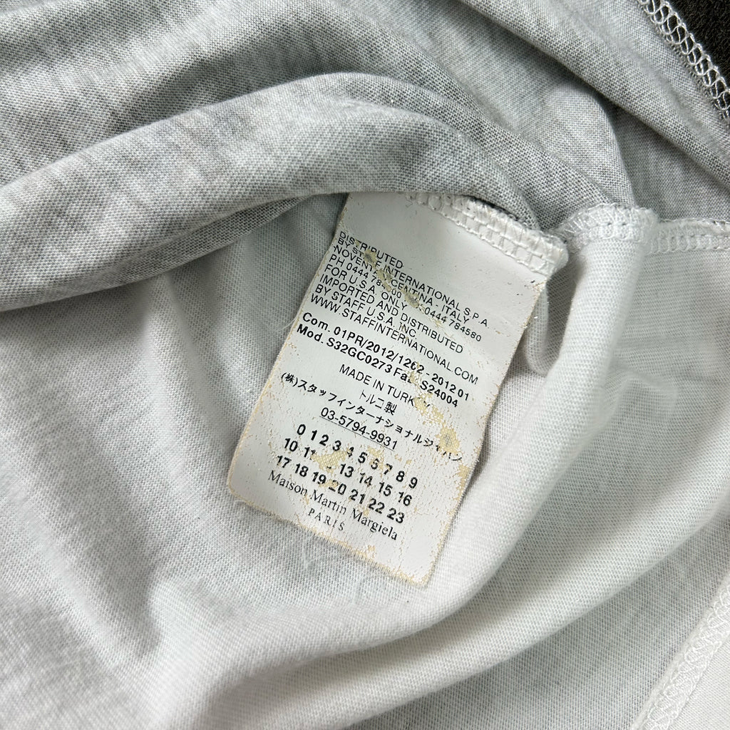 a close-up view of a white fabric, possibly a piece of clothing, with a small, partially visible label attached to it. The label appears to contain text and numbers, but the image does not contain any other objects or text that can be described in detail.