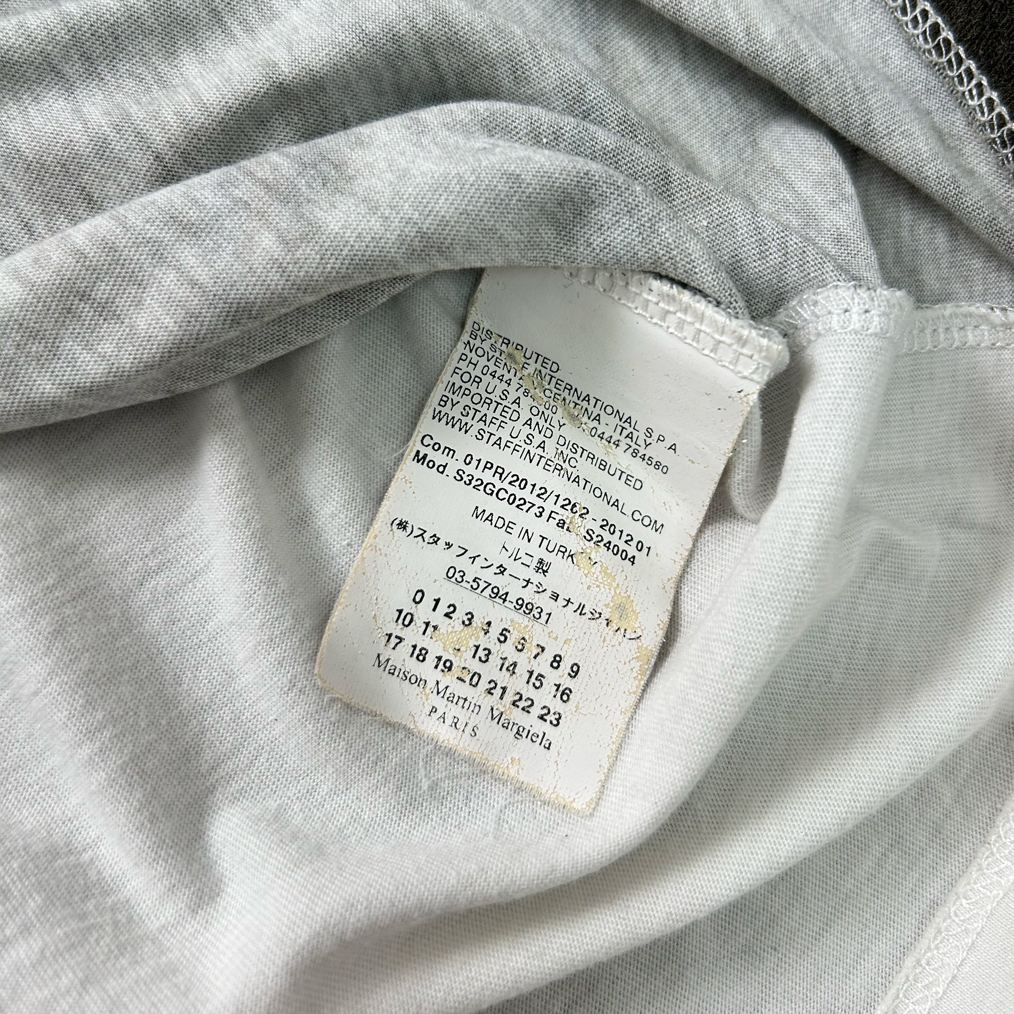 a close-up view of a white fabric, possibly a piece of clothing, with a small, partially visible label attached to it. The label appears to contain text and numbers, but the image does not contain any other objects or text that can be described in detail.