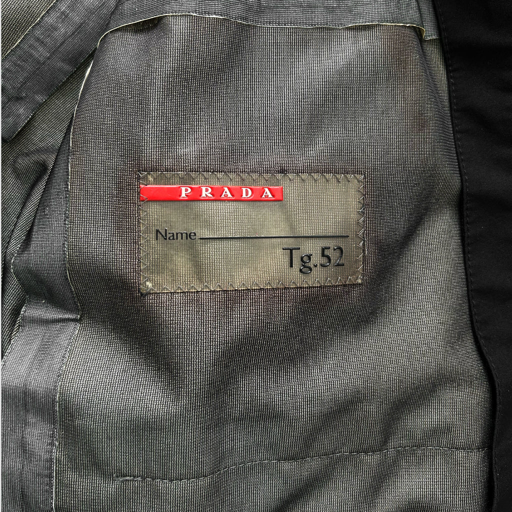 a gray fabric with a red label on it, which has the word "PRADA" printed on it. The label also has the name "Name" and the number "Tg52" printed on it.