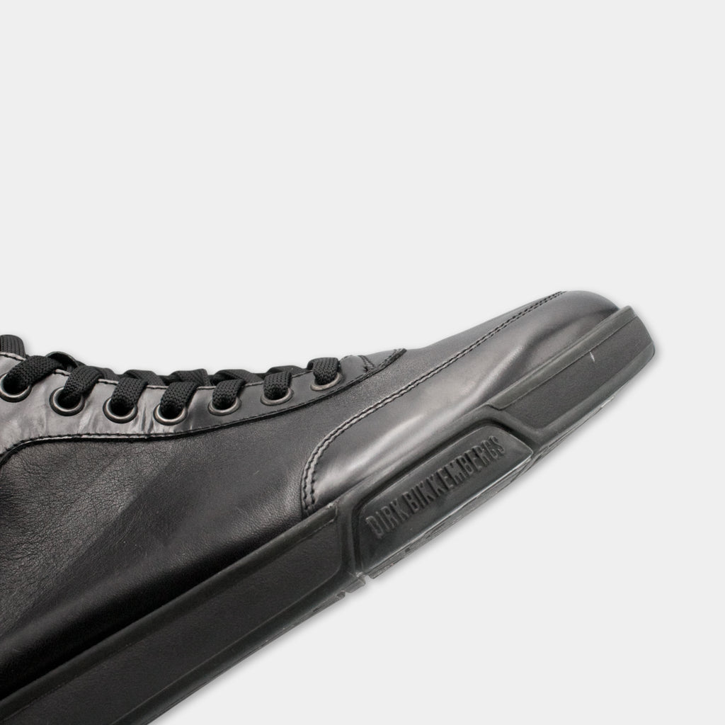 A close-up view of a black leather sneaker with a black sole and laces.