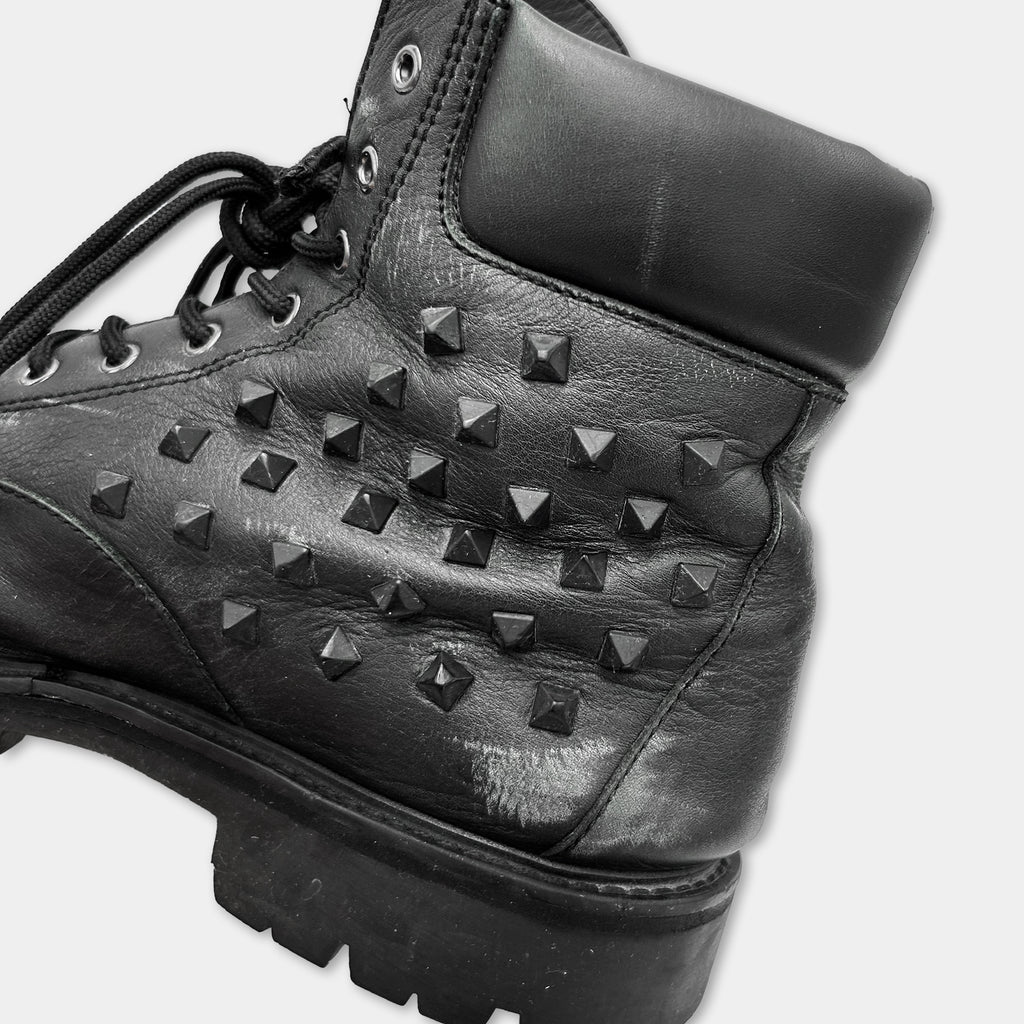 A close-up black and white image of a leather boot with a distinctive studded pattern.