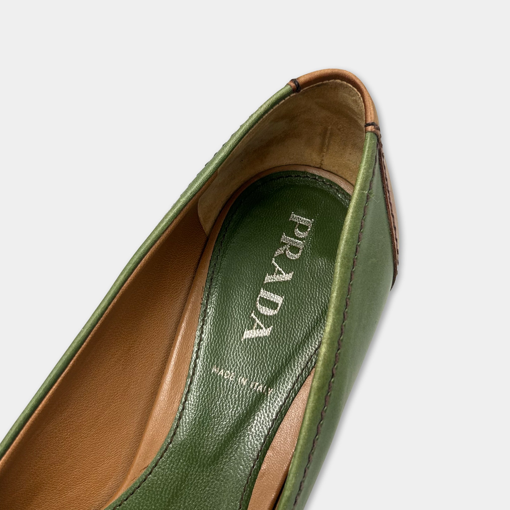 A close-up view of a green and brown shoe sole with the word "PRADA" printed on it.