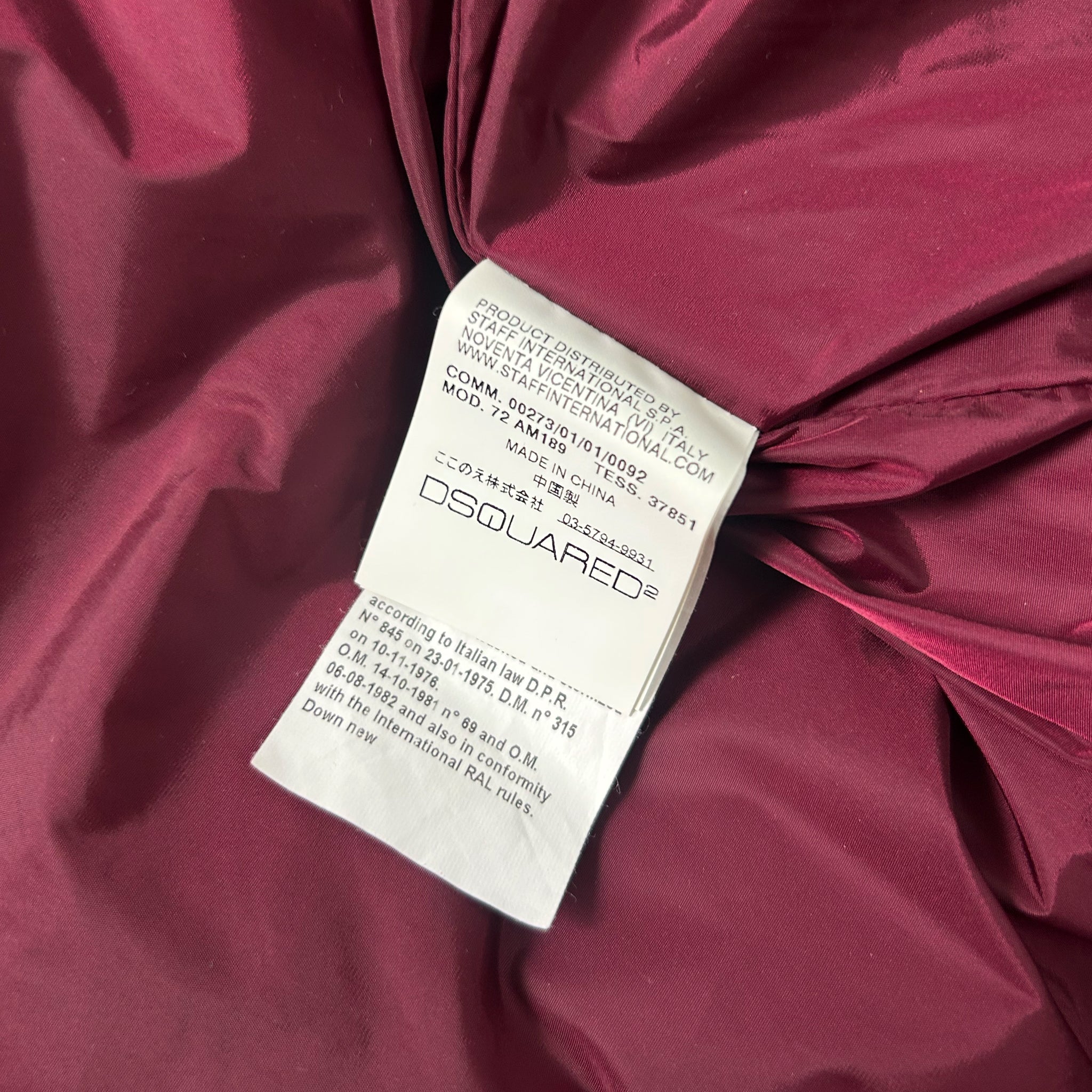 a close-up view of a red fabric, possibly a piece of clothing, with a label attached to it. The label appears to be a product label or tag, providing information about the product.