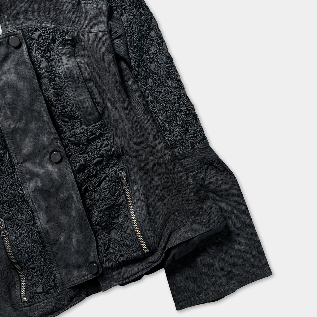 A close-up view of a black jacket with a lace-like pattern on the sleeves and zipper.