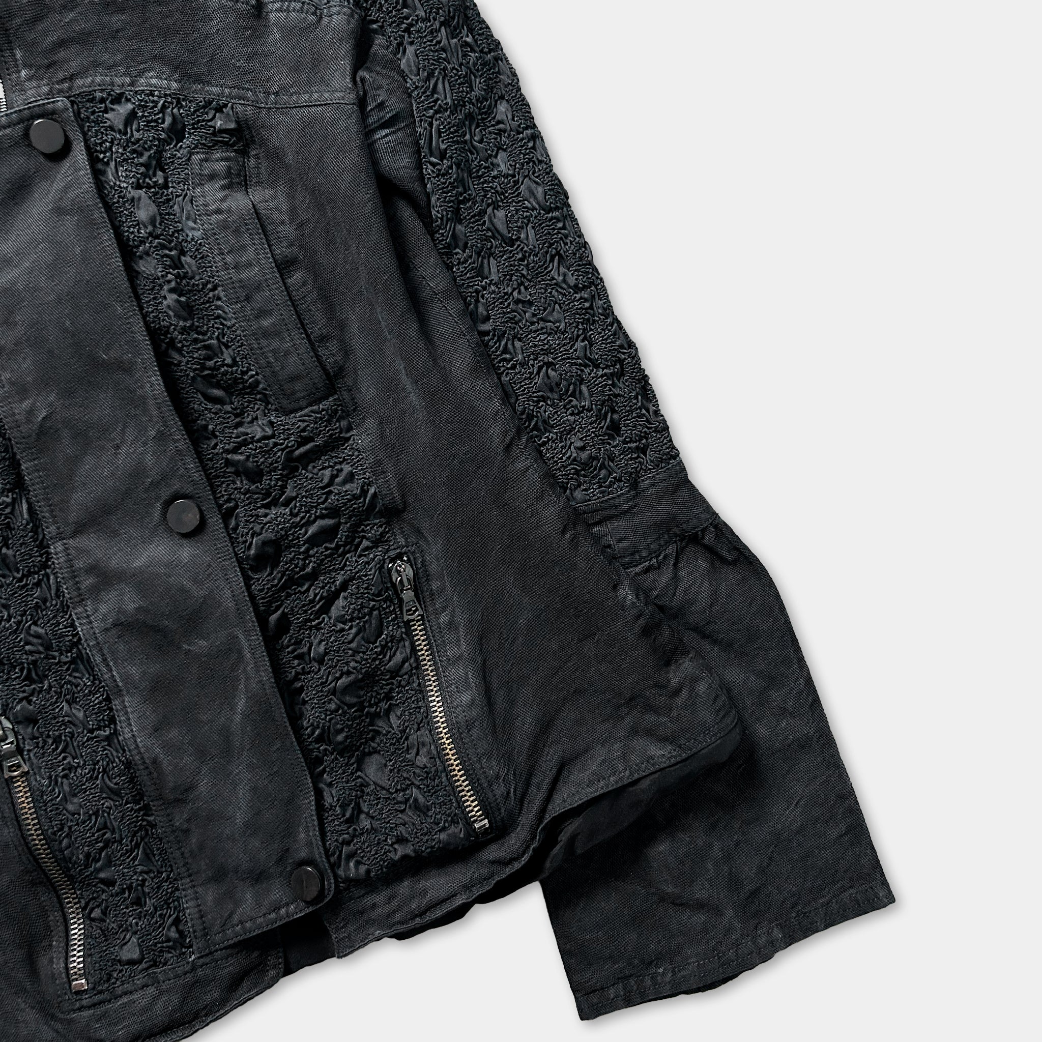 A close-up view of a black jacket with a lace-like pattern on the sleeves and zipper.