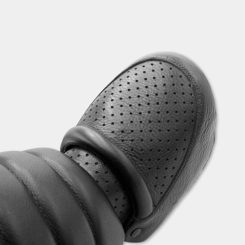 A close-up view of a black leather shoe with a perforated pattern on the side.