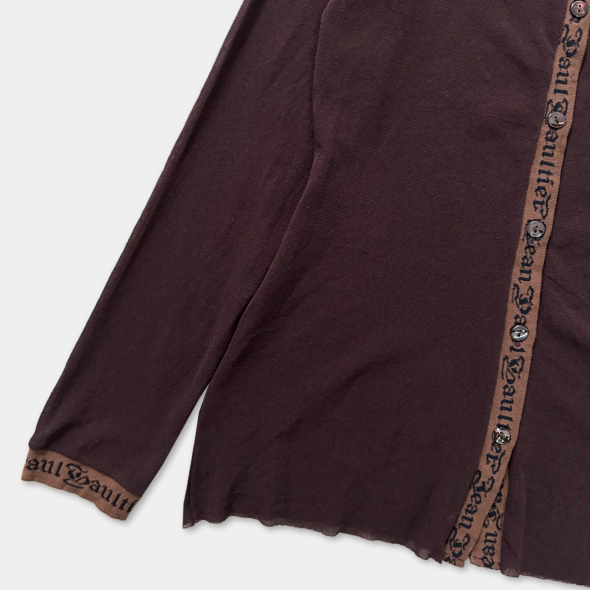 A close-up view of a dark brown long-sleeved garment with a brown trim, featuring a repeating pattern of text or design on the fabric.