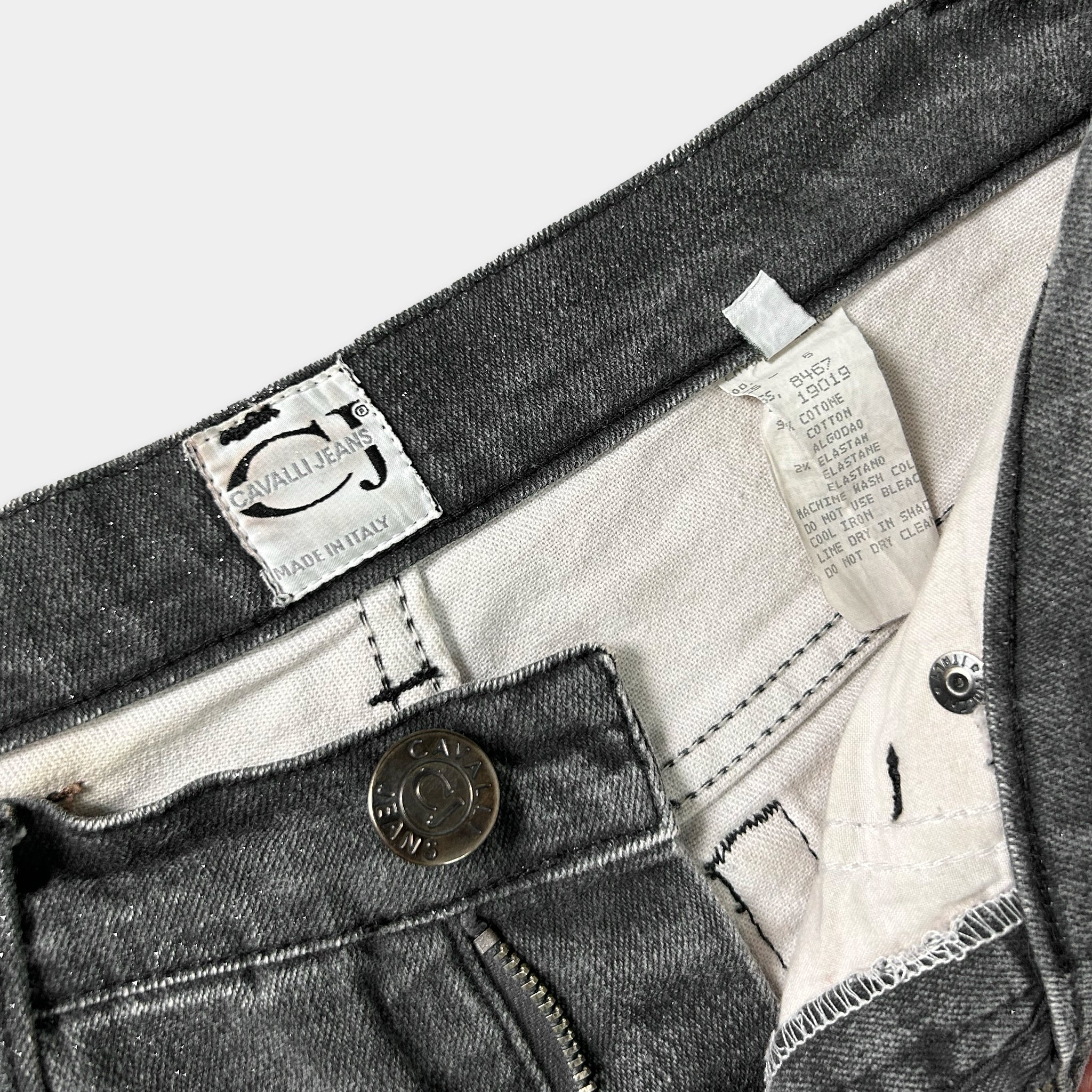 a close-up view of a pair of gray jeans, with a label on the waistband and a zipper visible.