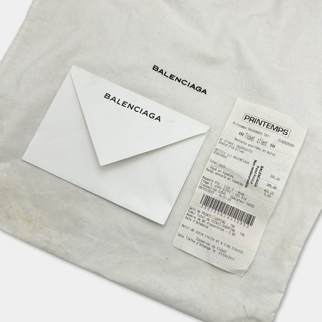 A white envelope and a white shopping bag with a Balenciaga logo are placed on a white surface.