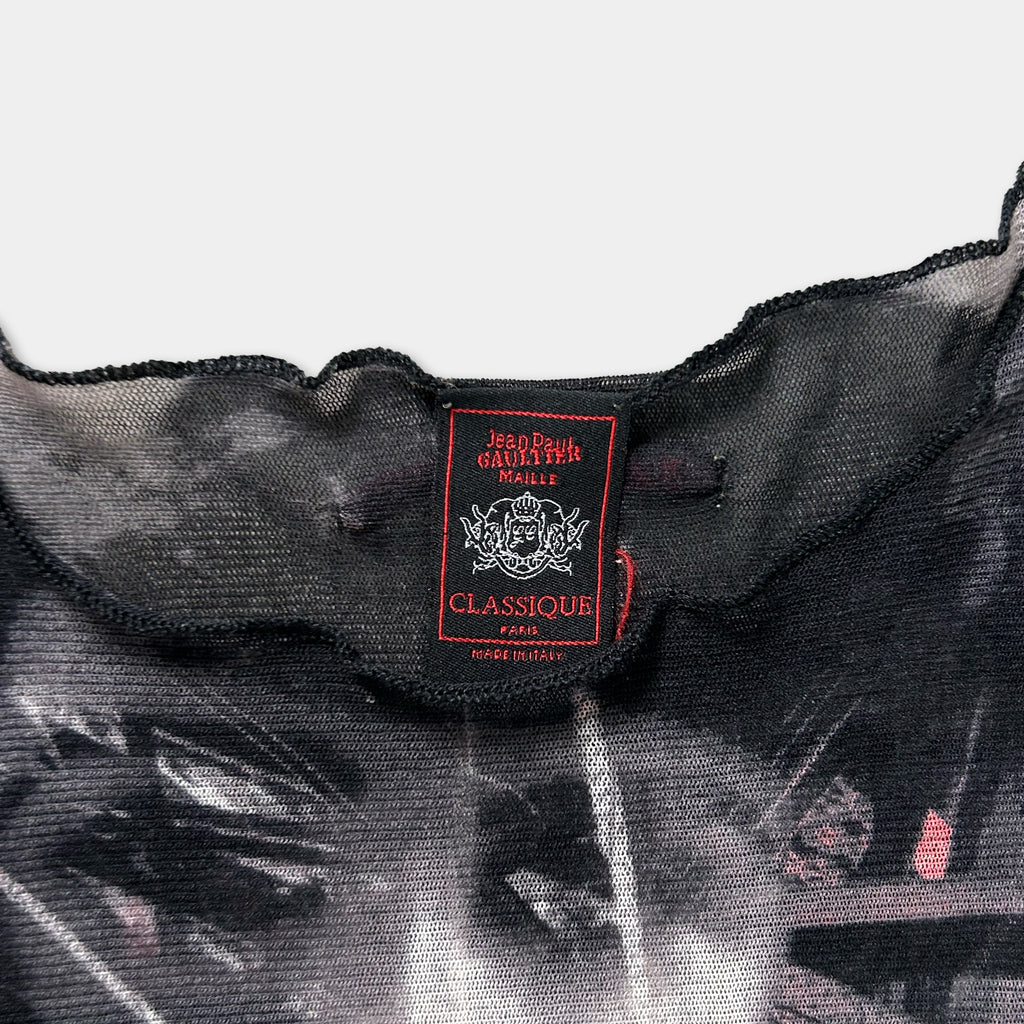 a close-up view of a black and gray patterned fabric, possibly a sheer or sheer-like material. There is a red and white label attached to the fabric, which appears to be a label or tag for the clothing item.