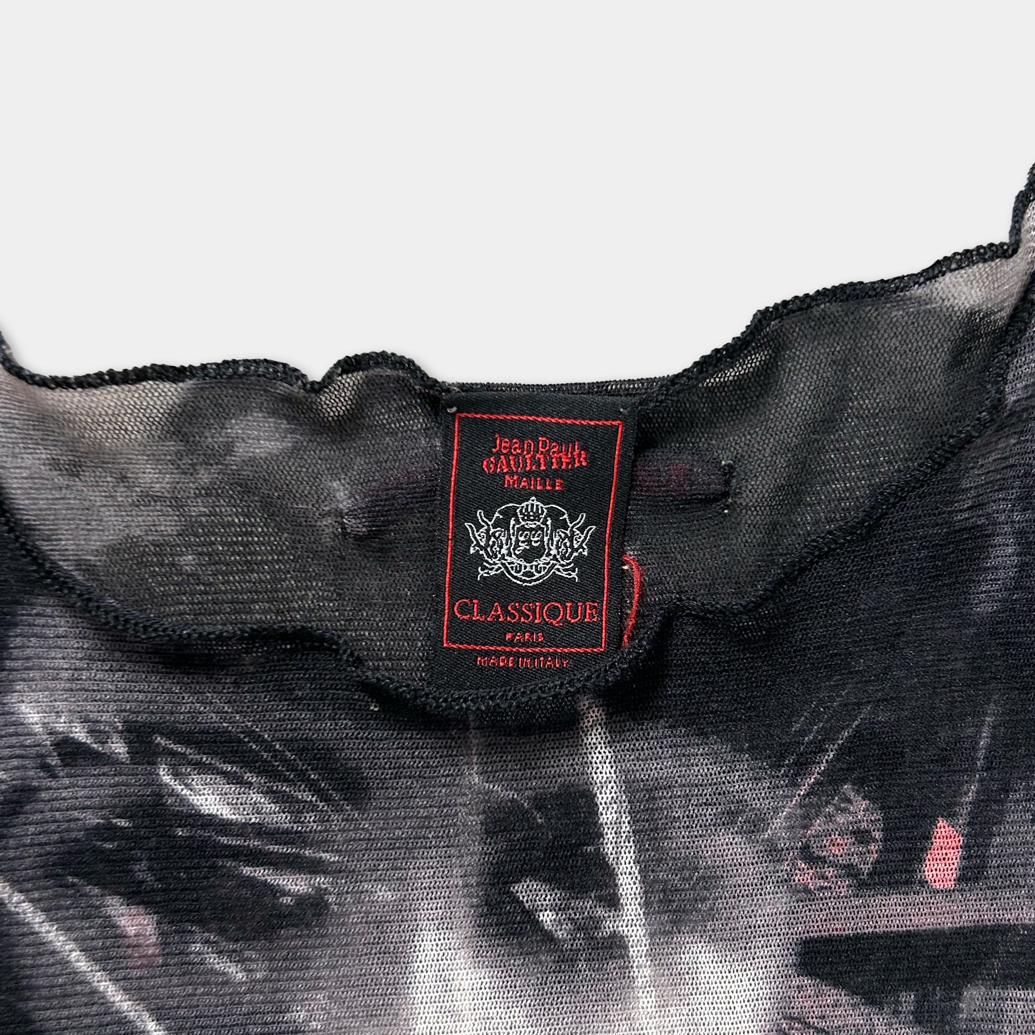 a close-up view of a black and gray patterned fabric, possibly a sheer or sheer-like material. There is a red and white label attached to the fabric, which appears to be a label or tag for the clothing item.