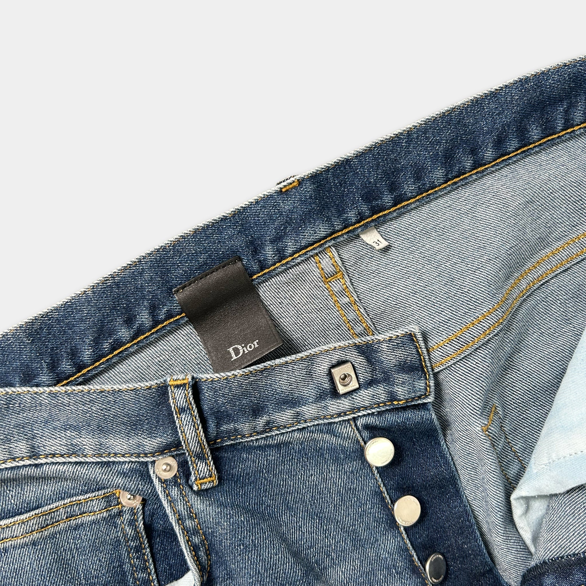 A close-up view of a pair of blue denim jeans with a Dior brand tag attached to the waistband.